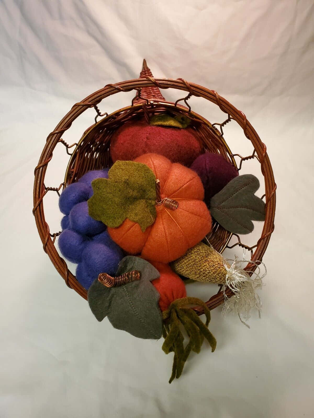 Fall Cornucopia 桌布 壁紙 — 一個編織籃子，裝滿了秋日色調的氈製南瓜、葡萄和葉子，背景為白色。