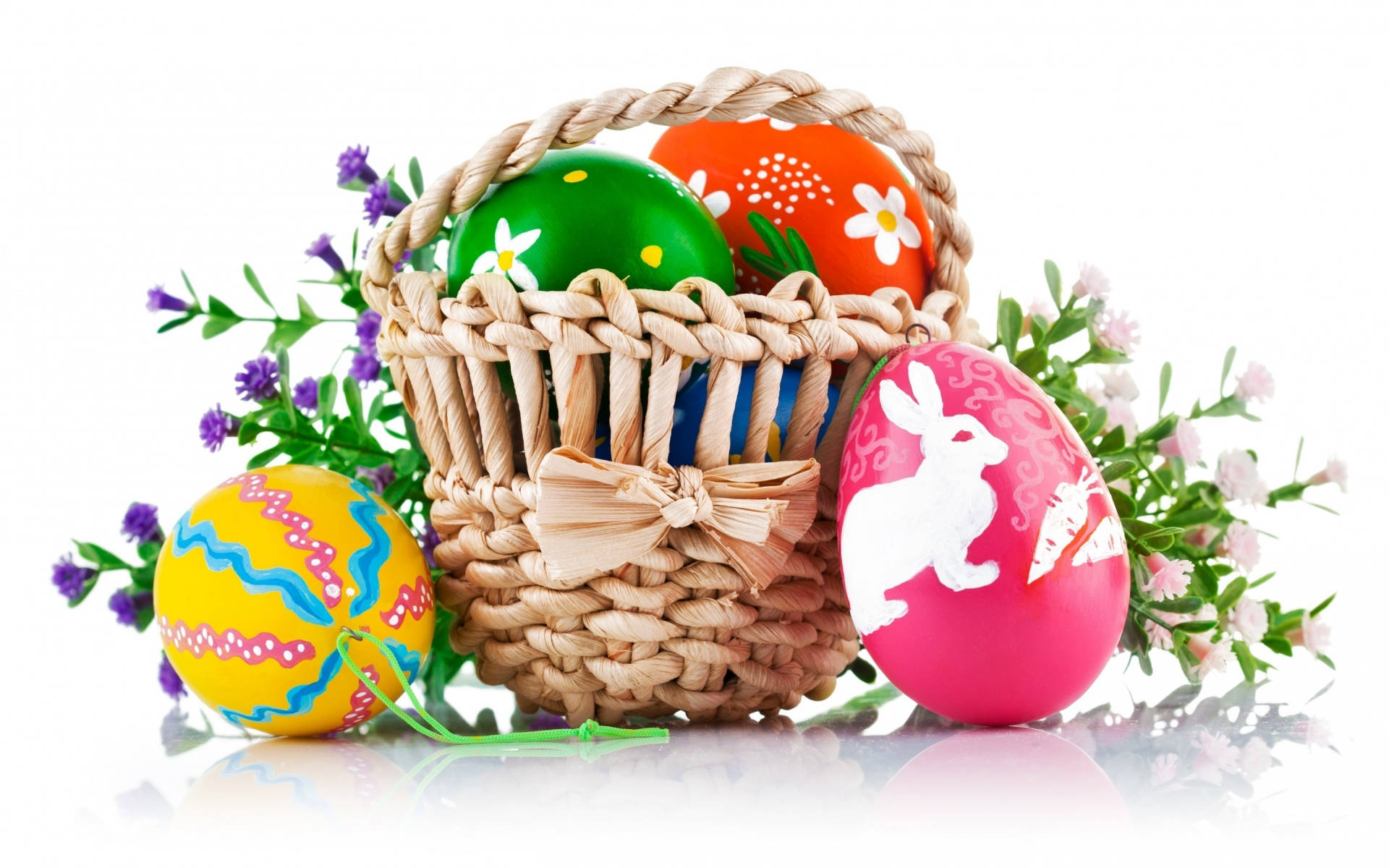 Cute Easter 桌布 壁紙 — 一個編織籃子，裝滿色彩鮮豔的復活節彩蛋和新鮮的春天花朵，背景是潔淨的白色。