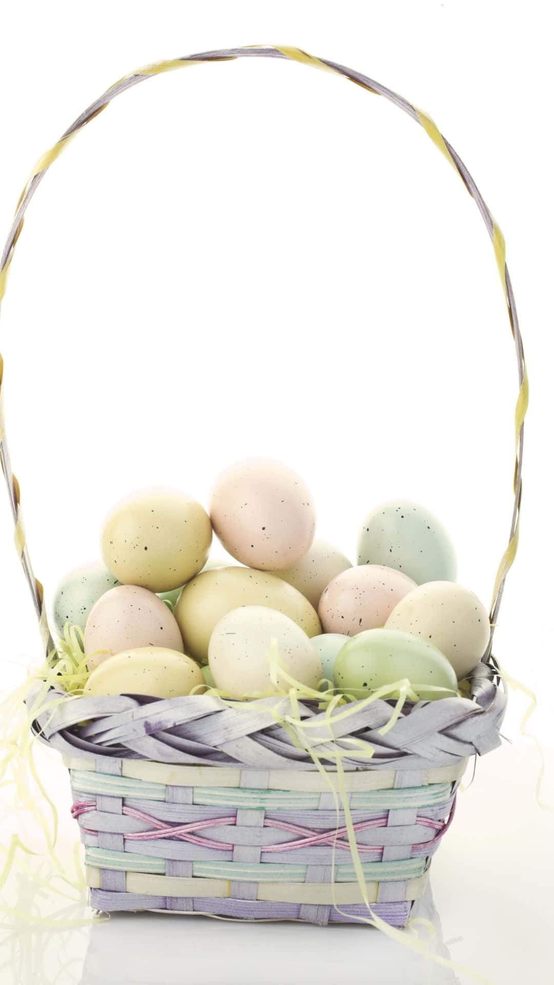 Easter Basket 桌布 壁紙 — 一個編織籃子，裡面裝滿了粉彩斑點復活節蛋，放在黃色稻草上，背景為白色。