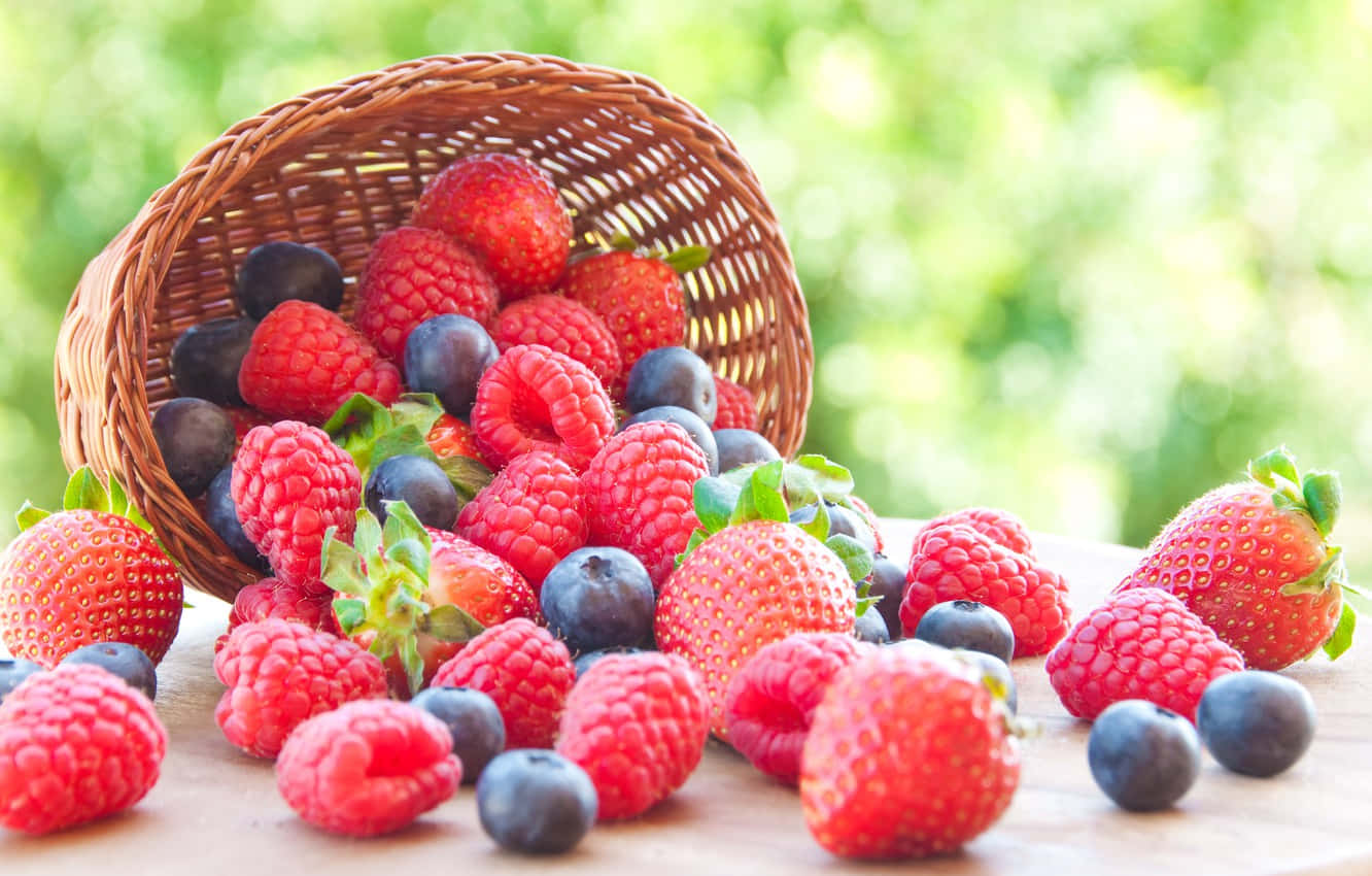 Raspberry 桌布 壁紙 — 一個編織籃子將鮮紅色的覆盆子、草莓和藍莓灑在木質表面上，背景是柔和的綠色模糊。
