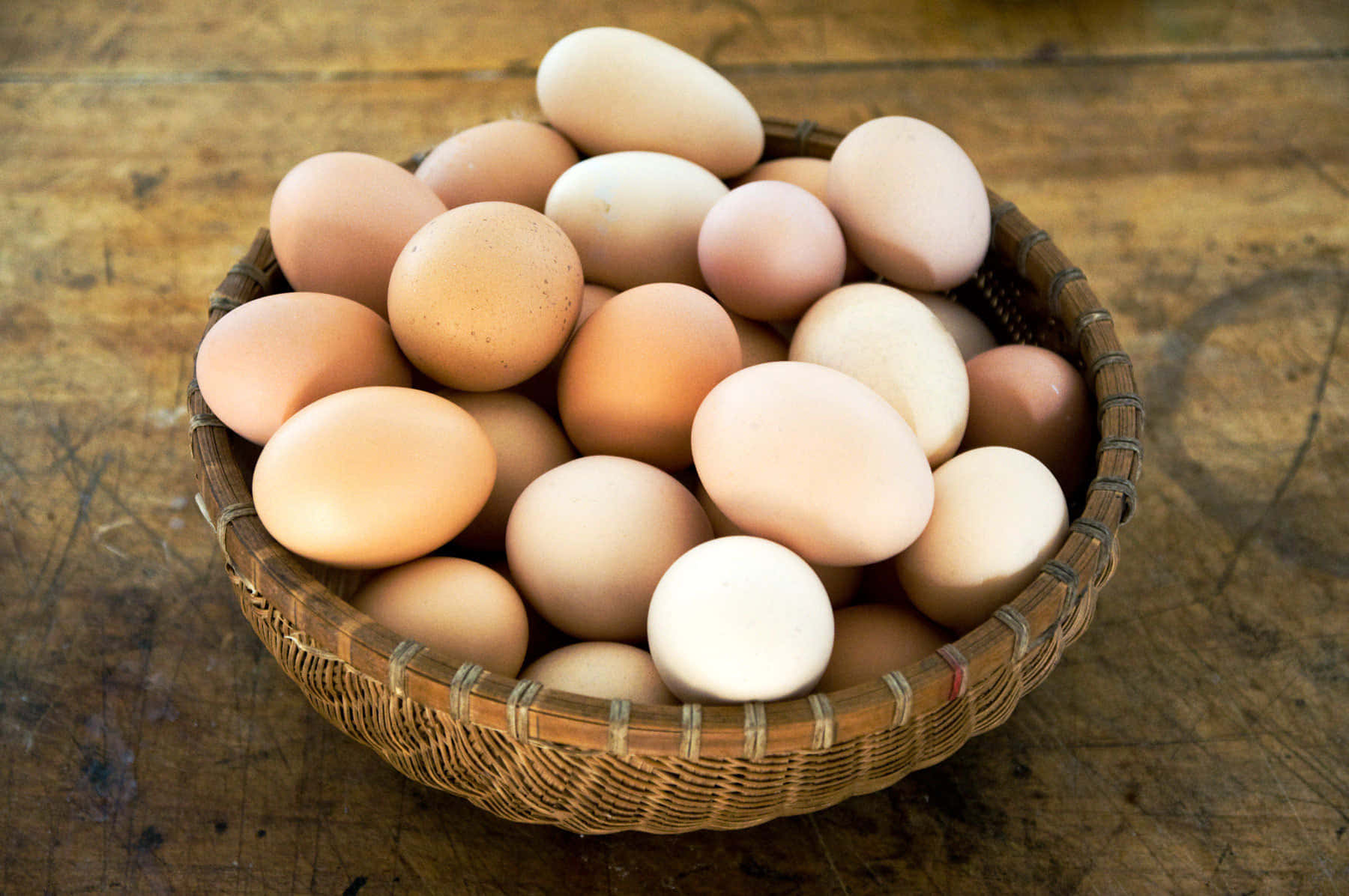 Egg 桌布 壁紙 — 一個編織籃子裝滿了各種棕色和白色的雞蛋，放在一張風化的木桌上。