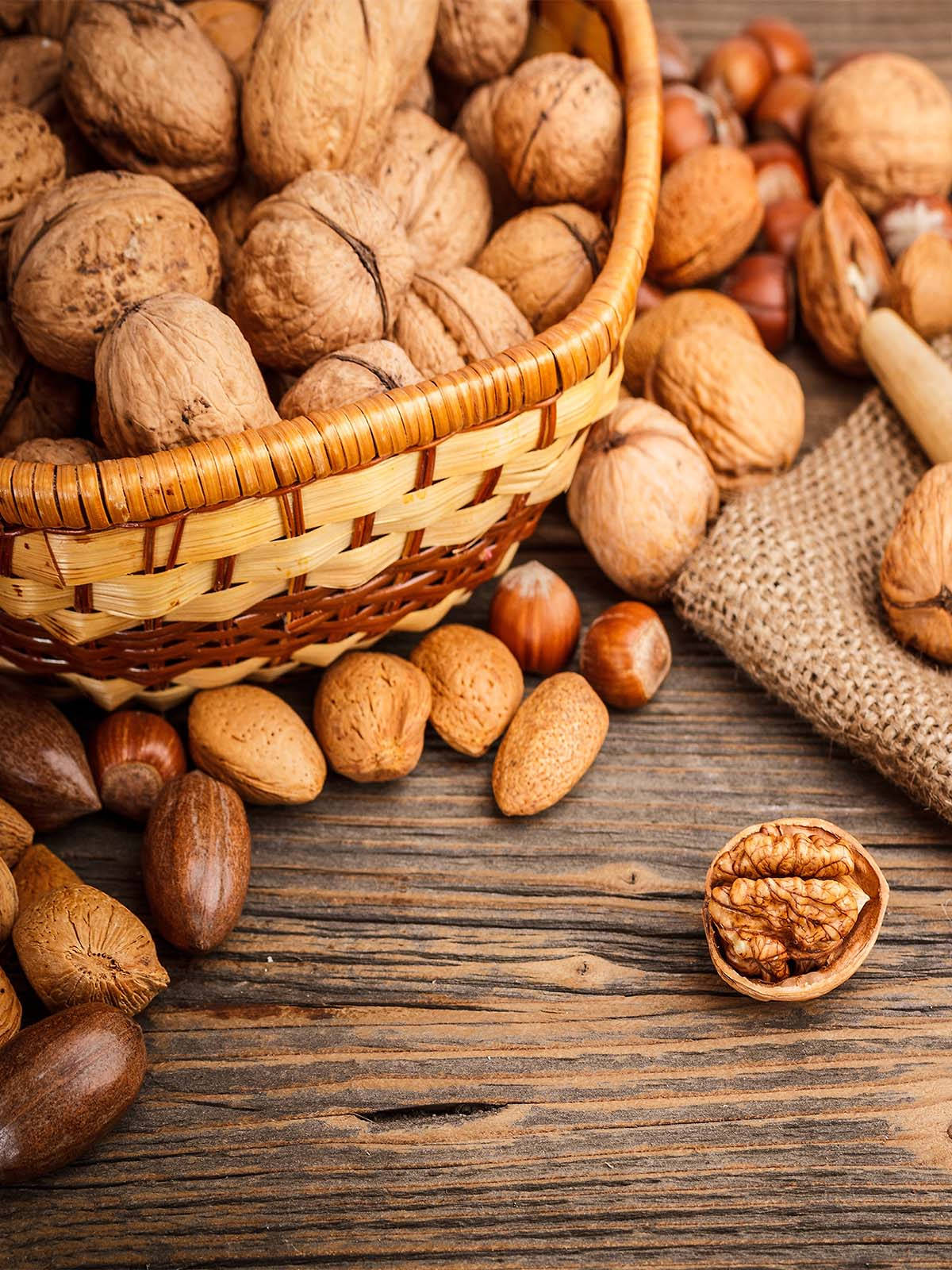 Almond 桌布 壁紙 — 一個編織籃子裝滿了核桃、榛子和杏仁，放在一個質樸的木桌上，旁邊有一塊粗麻布。