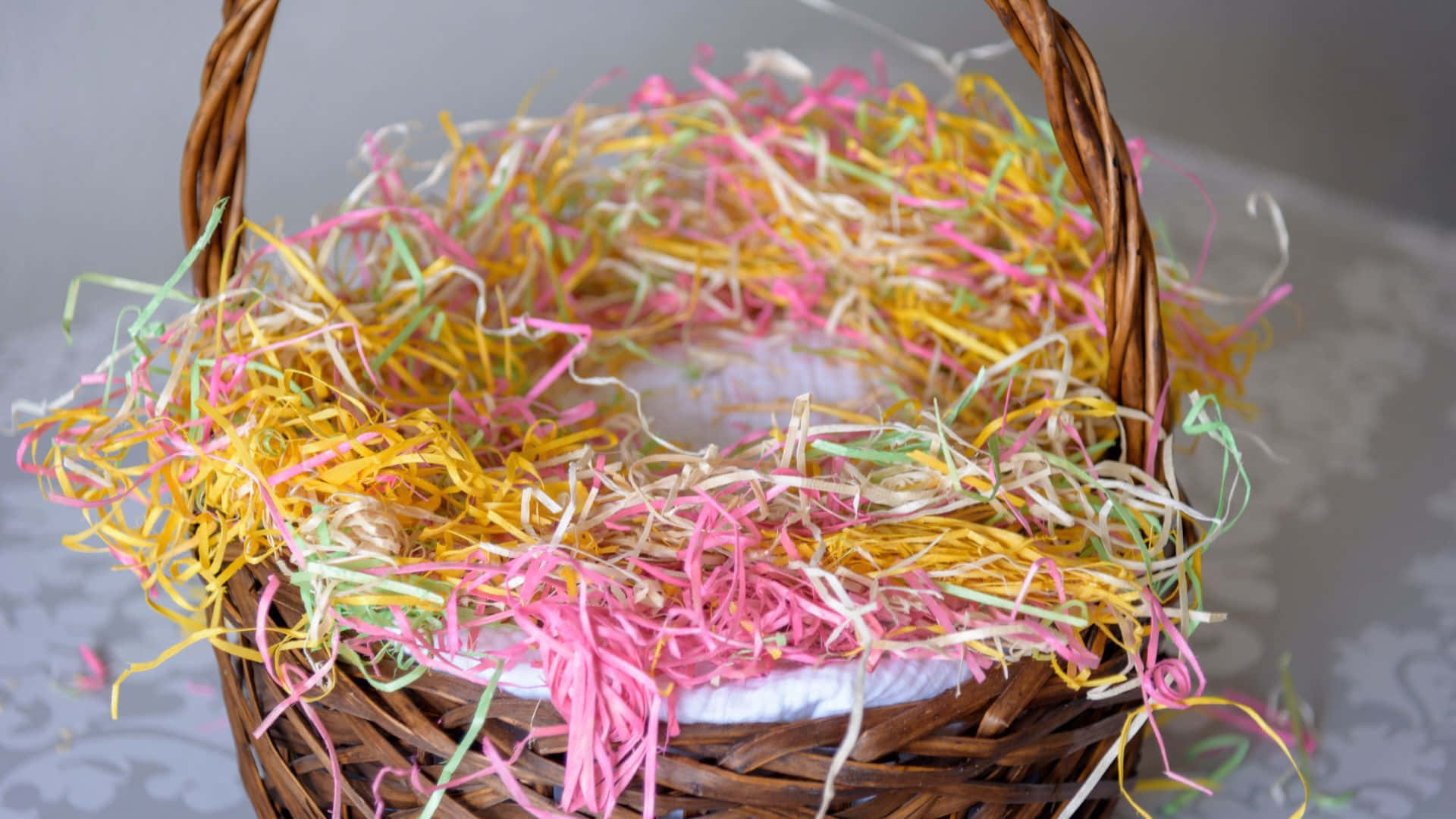 Easter Basket 桌布 壁紙 — 一個編織籃子裝滿彩色柔和碎紙，放在有圖案的表面上。