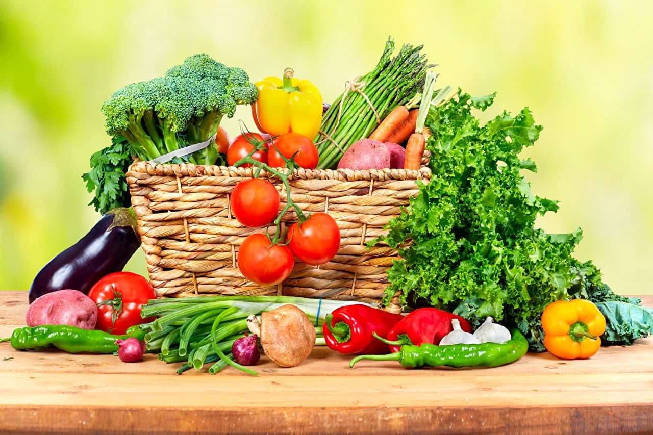 basket 桌布 壁紙 — 一個編織籃子裝滿新鮮色彩繽紛的蔬菜，如西蘭花、番茄和胡蘿蔔，放在木桌上，背景是柔和的綠色。