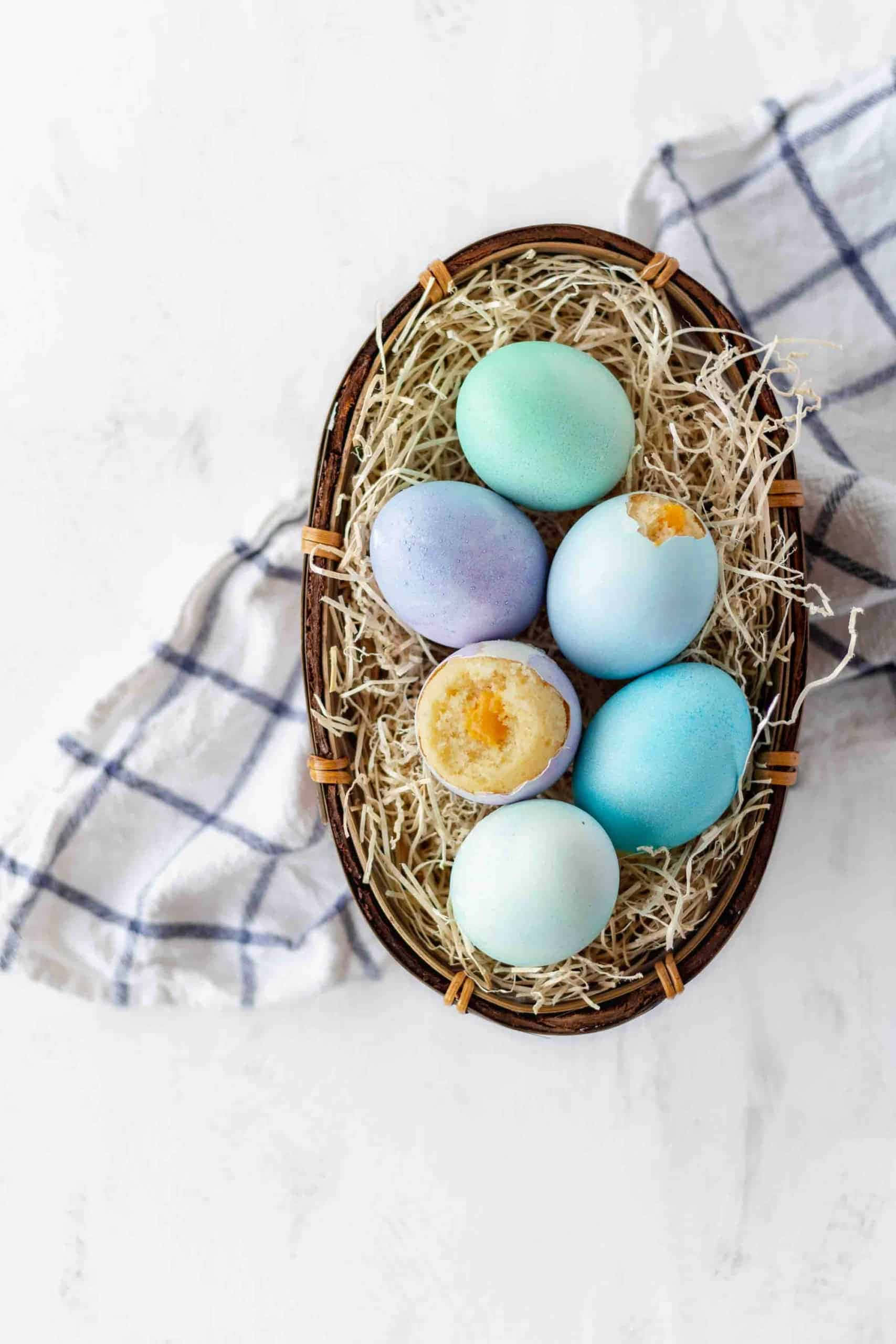 Eggshell 桌布 壁紙 — 一個編織籃子裝滿粉藍色和綠色復活蛋，有些裂開露出蛋黃，放在格子布上的稻草上。