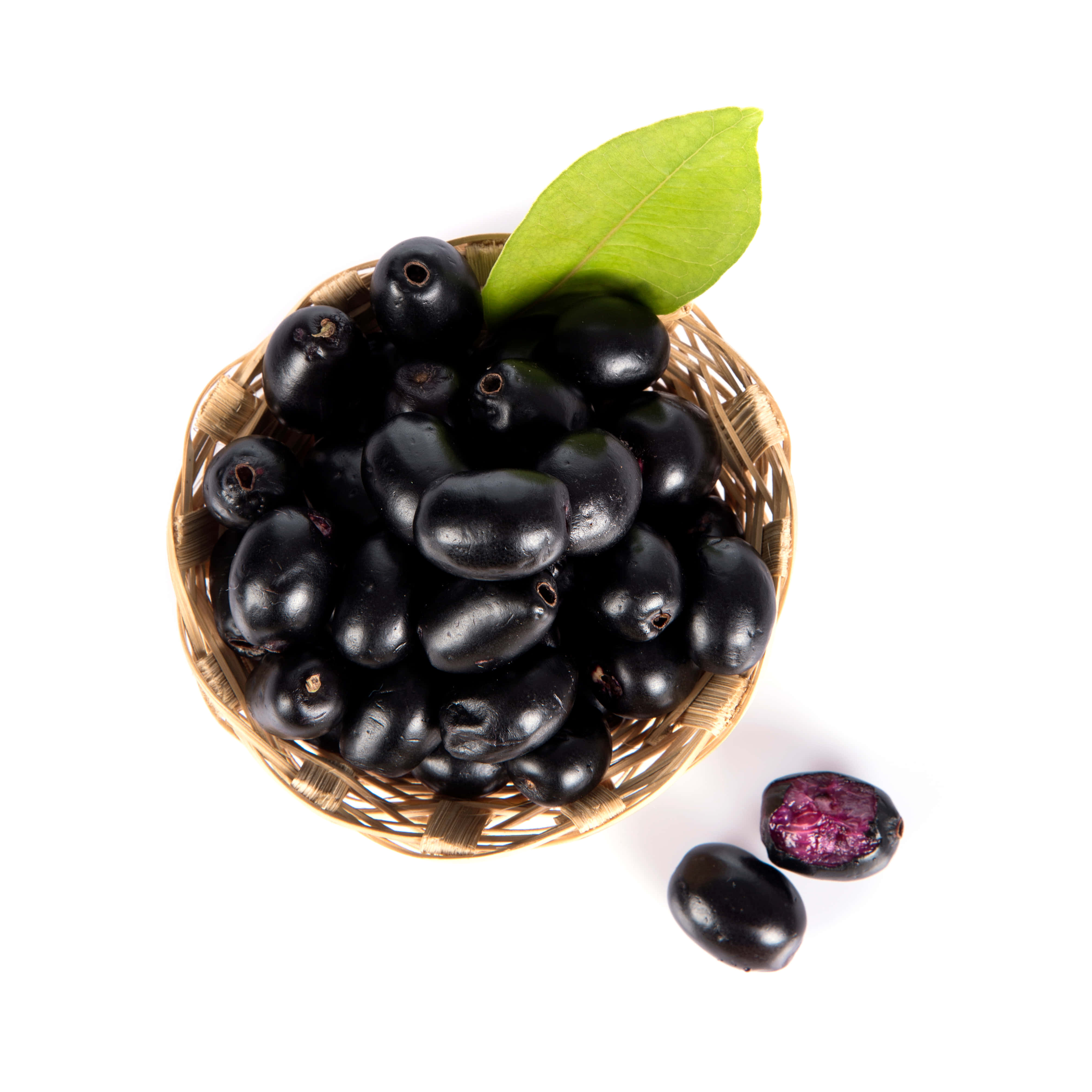 basket 桌布 壁紙 — 一個編織籃子裝著光澤的黑色詹布蘭果實，配上一片鮮綠色的葉子，旁邊有兩個切半的果實，露出紫色的果肉，放在白色背景上。