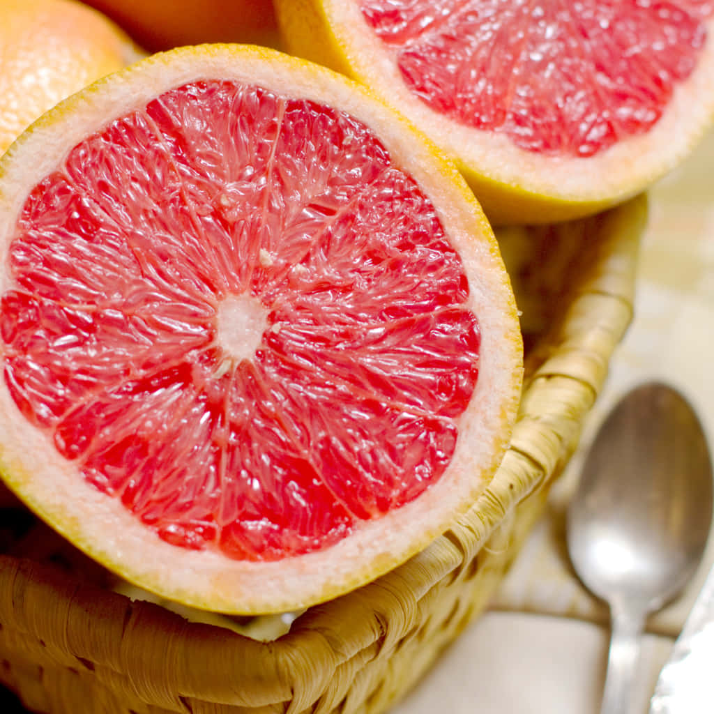 Pink Grapefruit 桌布 壁紙 — 一個編織籃子裡有鮮紅色葡萄柚半邊的特寫，旁邊放著一個湯匙。