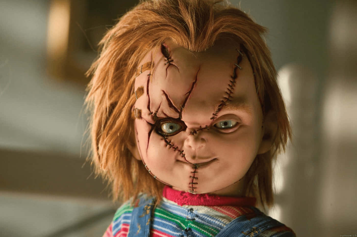 Chucky Doll 桌布 壁紙 — 一個縫製玩偶的特寫，擁有狂野的橙色頭髮和詭異的藍色眼睛，穿著條紋連身褲。