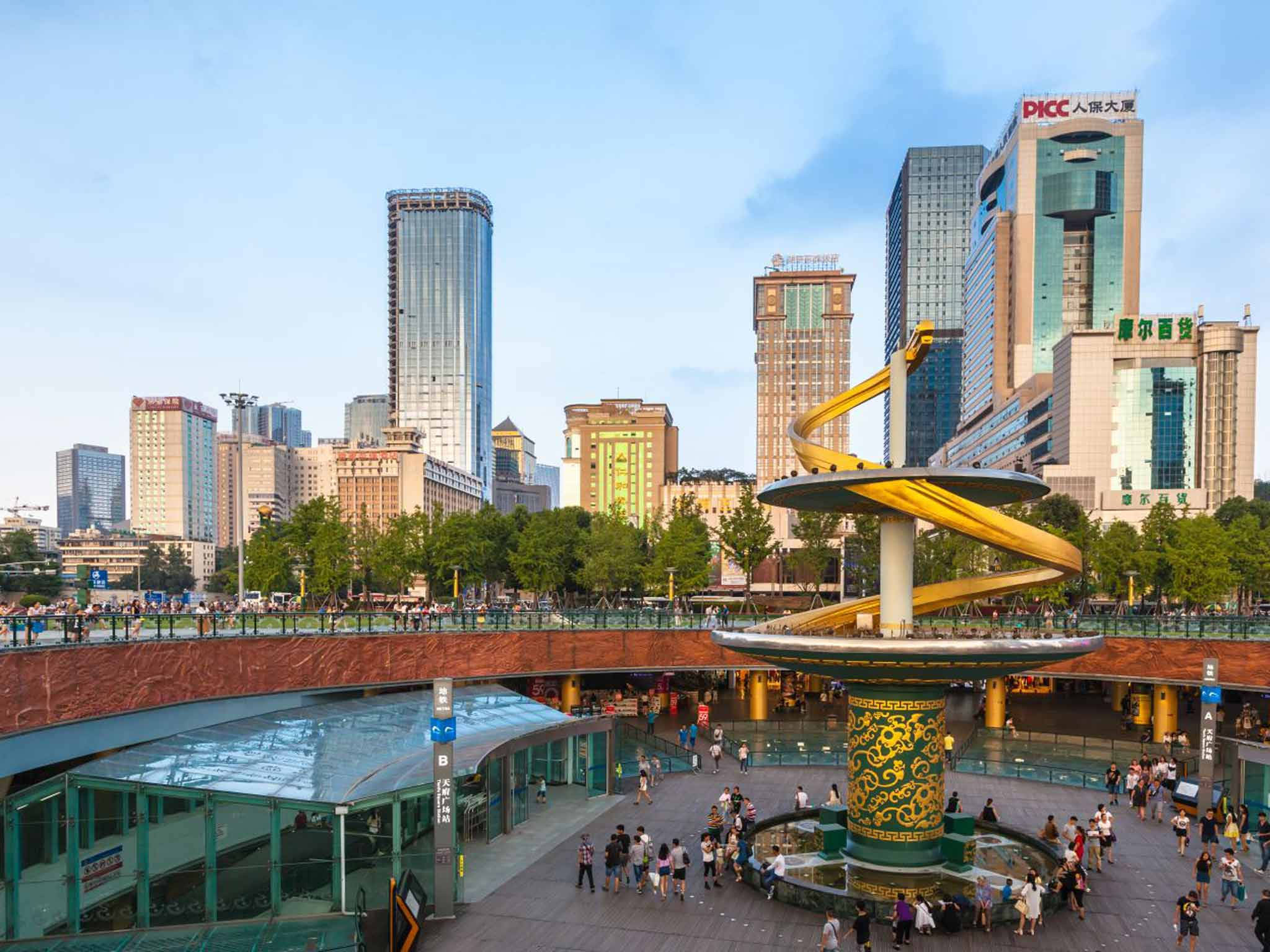 Chengdu 桌布 壁紙 — 一個繁忙的城市廣場上，有一座引人注目的金色螺旋雕塑，周圍有行人和現代摩天大樓，在晴朗的藍天下。