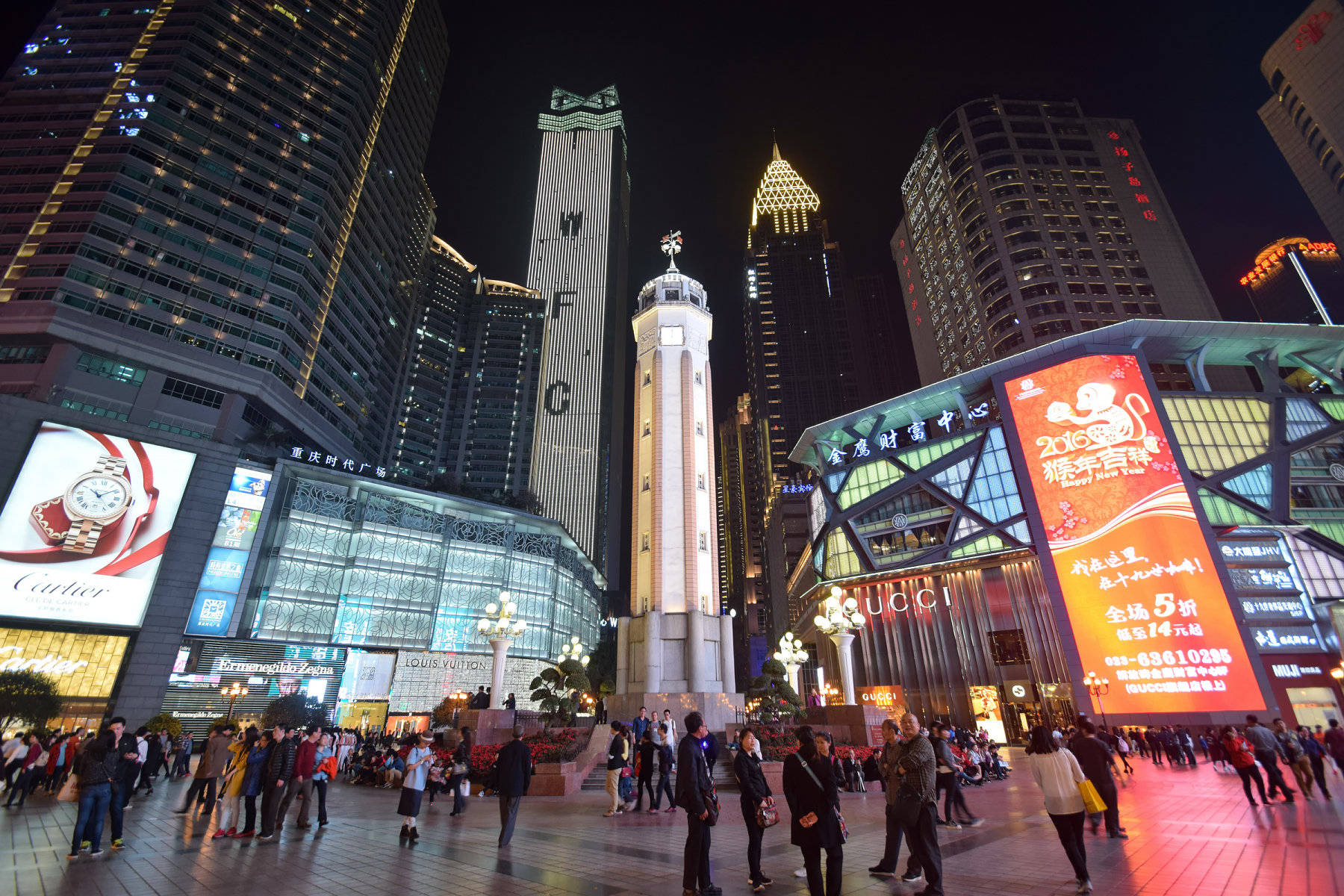 Chongqing 桌布 壁紙 — 一個繁忙的夜間城市廣場，擠滿人群和裝飾著發光廣告牌和霓虹燈的高聳摩天大樓。
