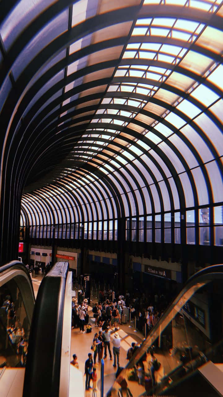 Airport 桌布 壁紙 — 一個繁忙的現代交通站，頭頂有彎曲的玻璃和鋼拱，人們在下面的自動扶梯和月台上移動。
