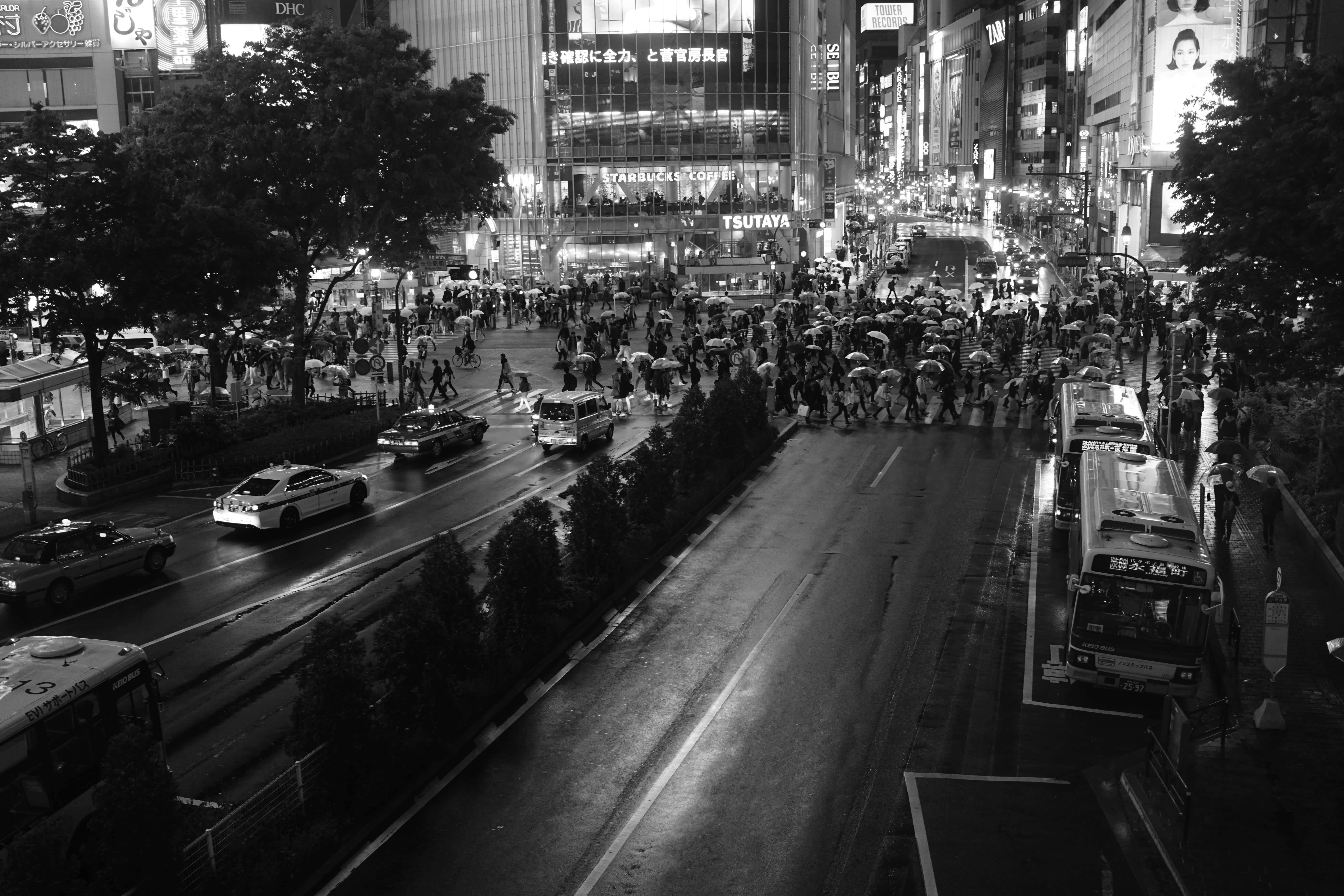 日本 桌布 壁紙 — 一個繁忙的雨夜，在霓虹燈閃爍的城市街道上，人群撐著傘穿過濕漉漉的馬路。