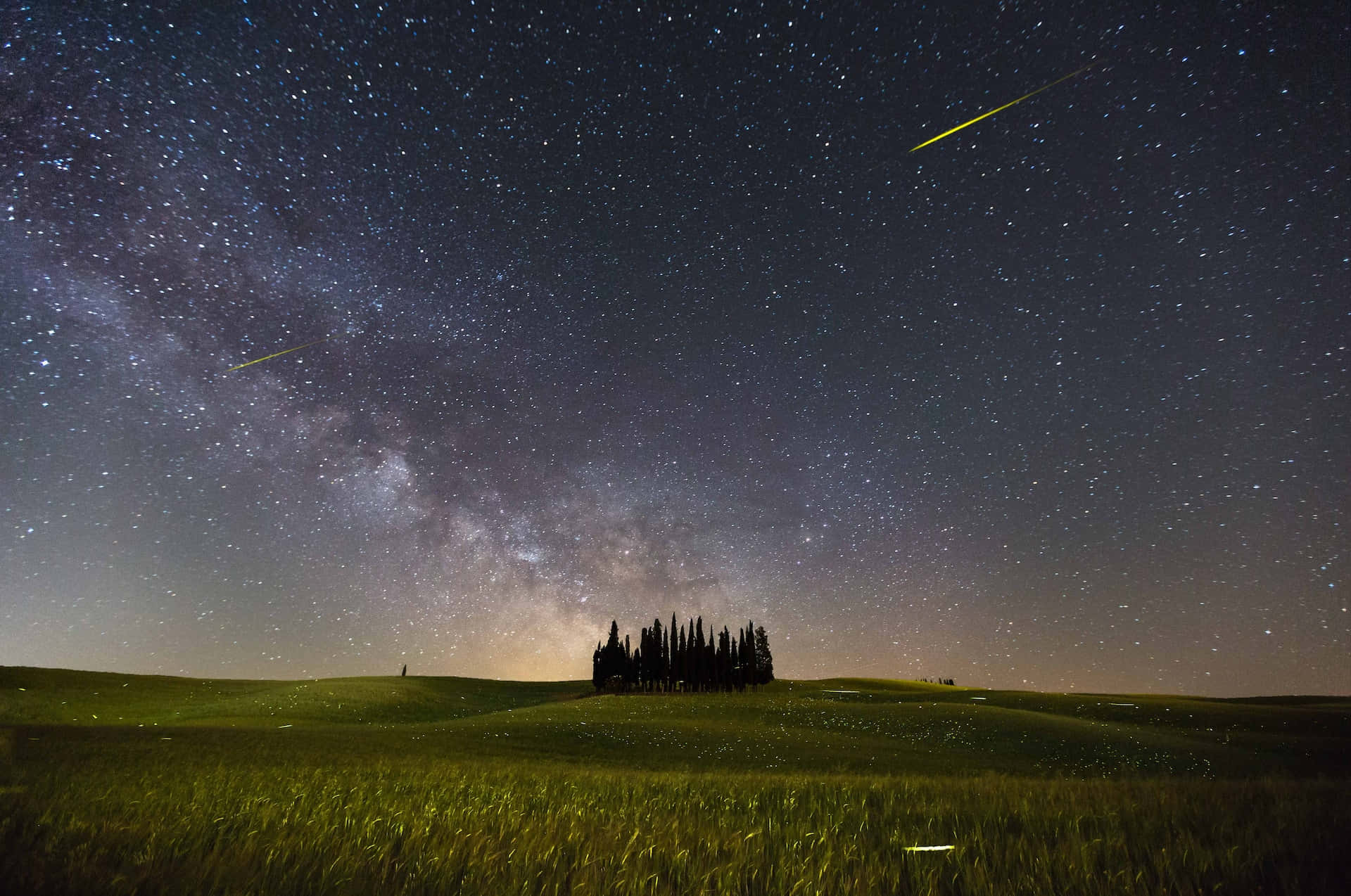 comet 桌布 壁紙 — 一個繁星點點的夜空，銀河和流星在長滿草的山丘上拱起一棵剪影的柏樹。