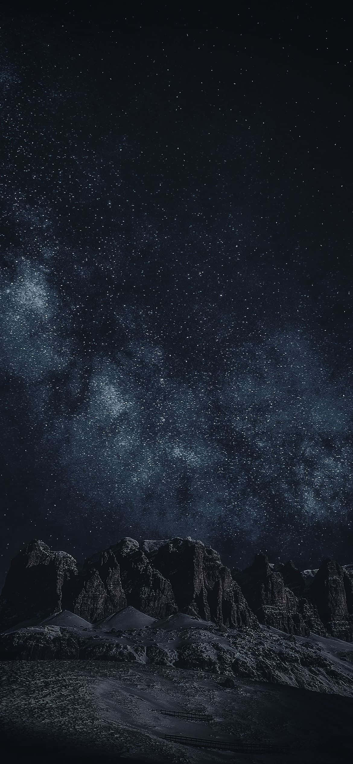 Black Space 桌布 壁紙 — 一個繁星點點的夜空，銀河在深靛藍和黑色調中拱起於崎嶇的山脈之上。