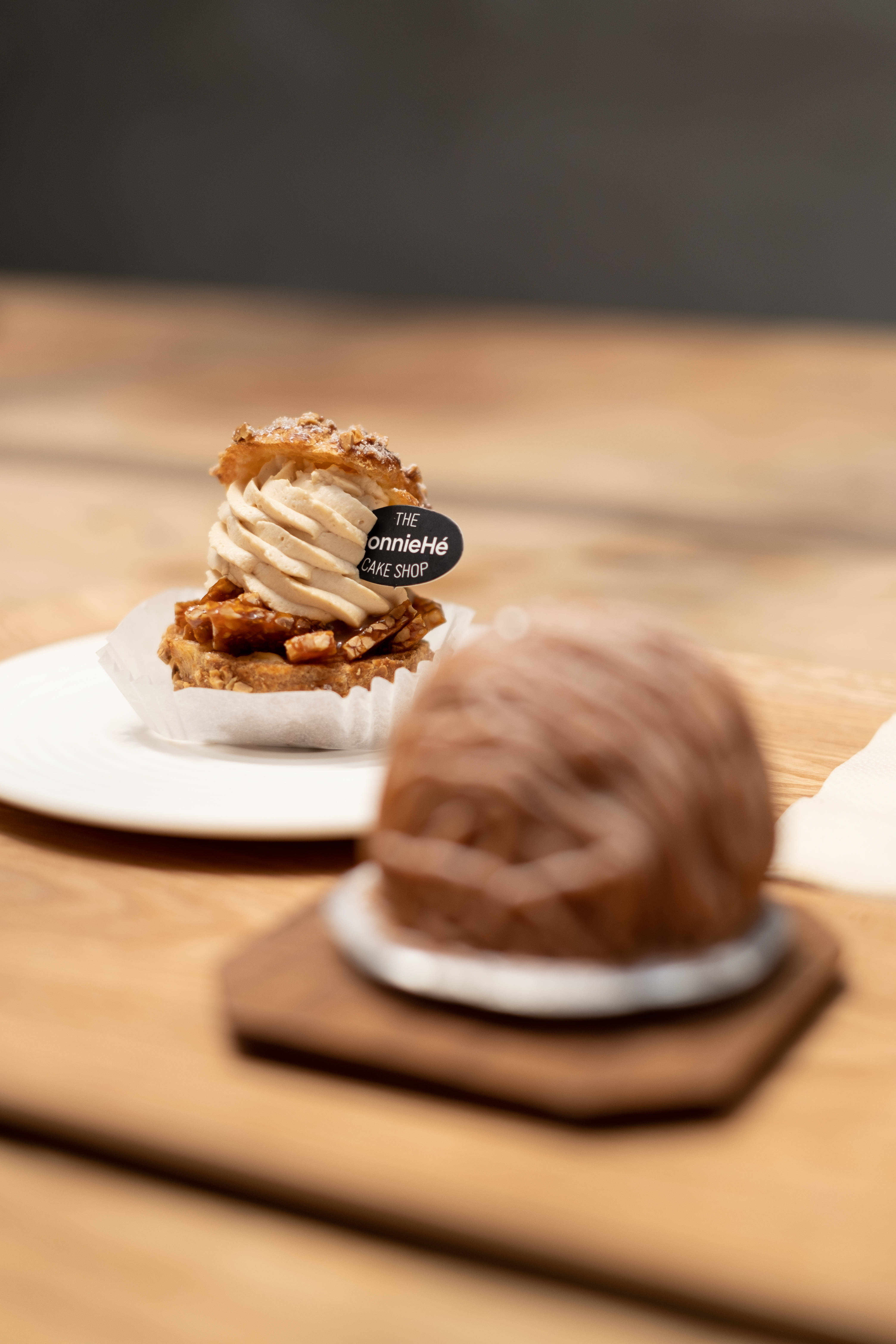 Pastry 桌布 壁紙 — 一個美味的焦糖奶油糕點帶有品牌標籤，焦點放在木桌上模糊的巧克力甜點旁邊。