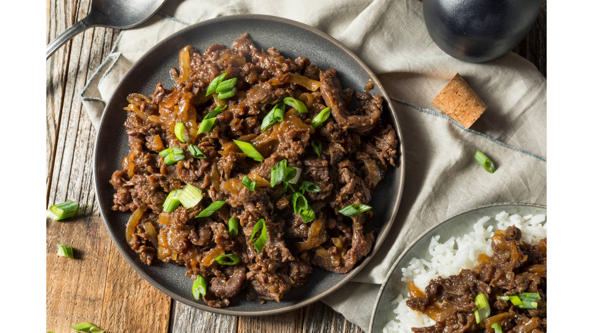Rice 桌布 壁紙 — 一個美味的牛肉洋蔥炒菜，上面撒上青蔥，放在一個深色碗裡，置於鄉村風格的木桌上。