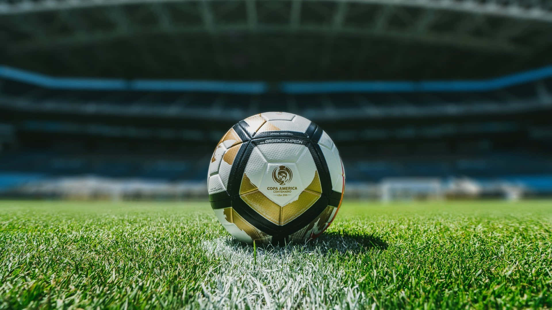 Soccer Ball 桌布 壁紙 — 一個美洲盃足球在明亮的日光下，放置在空蕩蕩的體育館中充滿活力的綠色草地上。