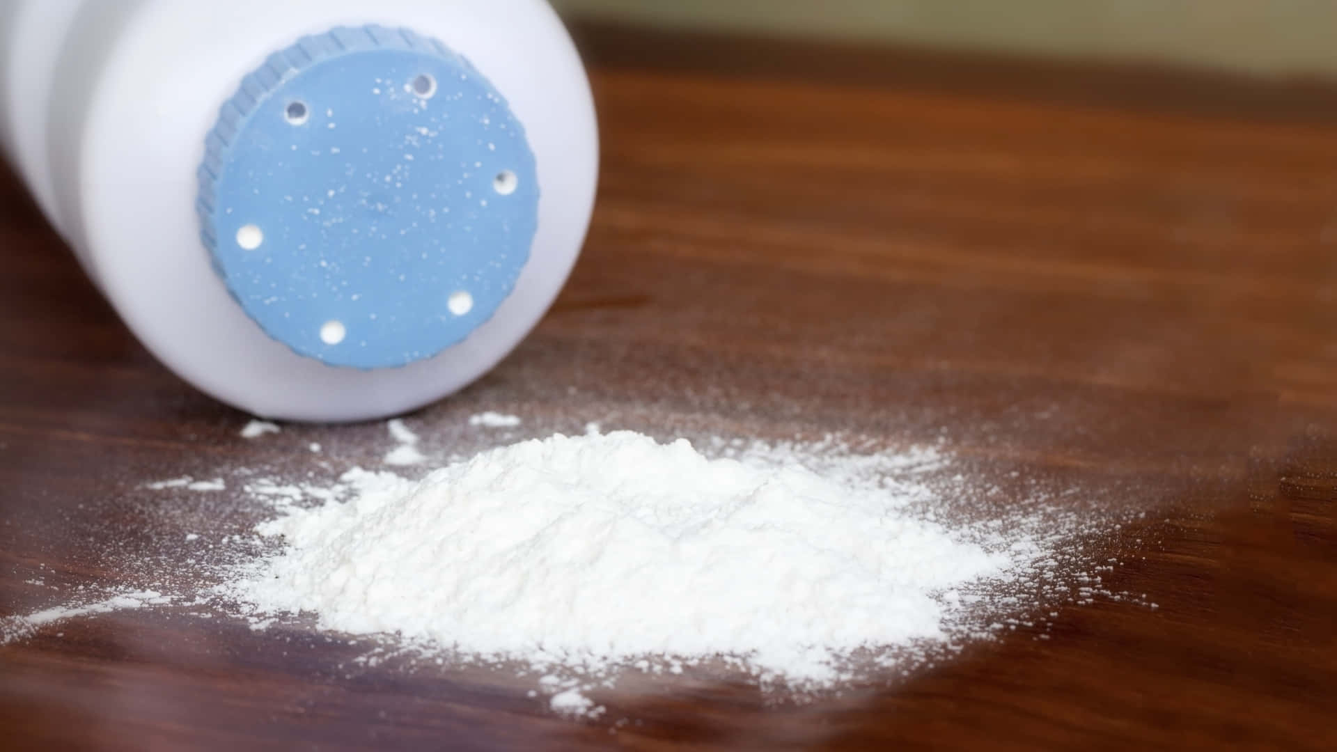 Baby Powder 桌布 壁紙 — 一個翻倒的白色粉末容器將細白粉末灑在暖色調的木質表面上。