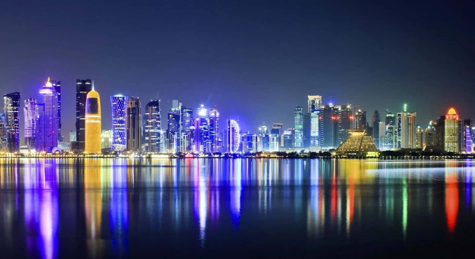 Qatar 桌布 壁紙 — 一個耀眼的夜景城市景觀，摩天大樓在霓虹色調中發光，完美地倒映在平靜的水面上。