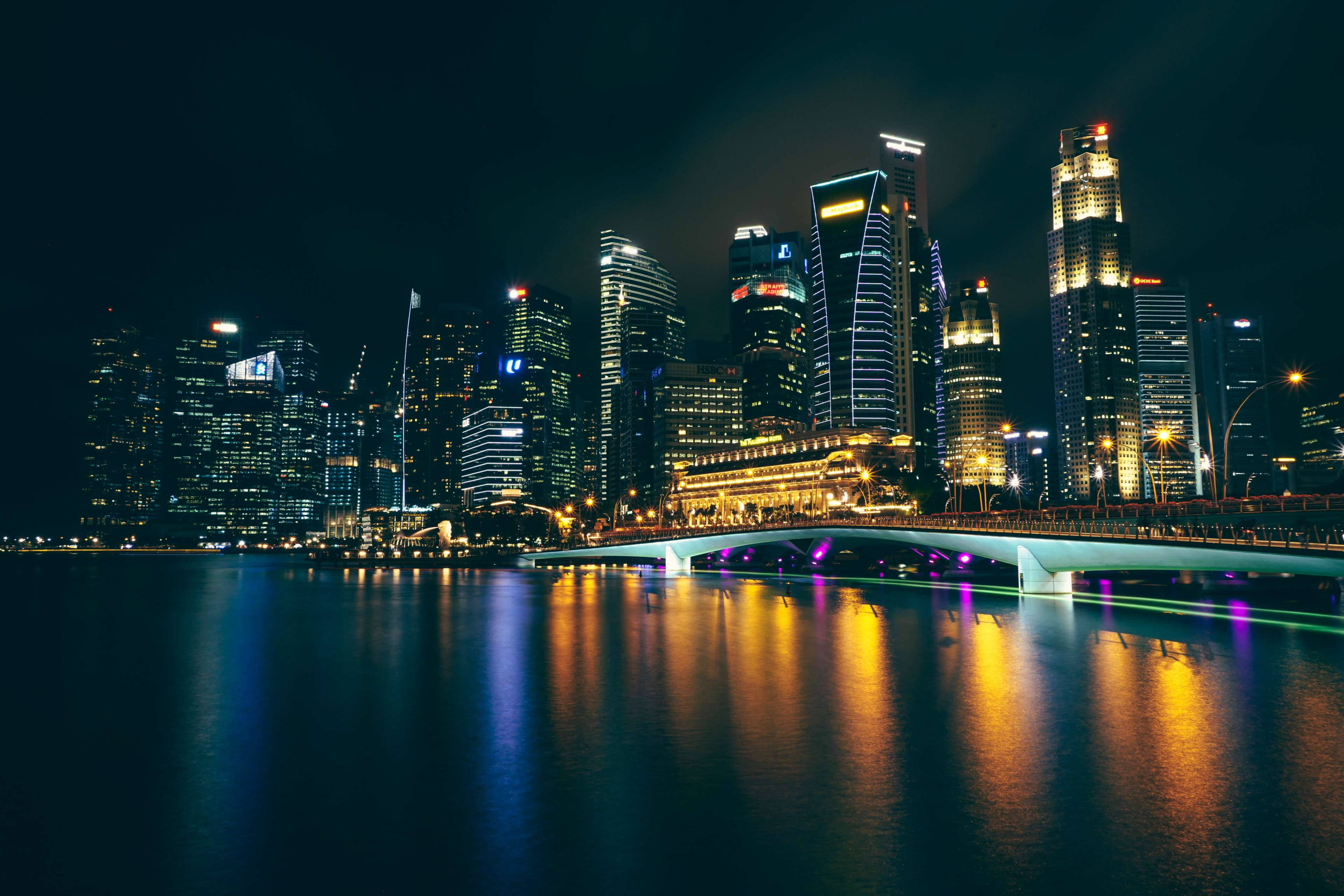 City At Night 桌布 壁紙 — 一個耀眼的夜景城市景觀，有燈火通明的摩天大樓和一座發光的橋樑倒映在平靜的水面上。