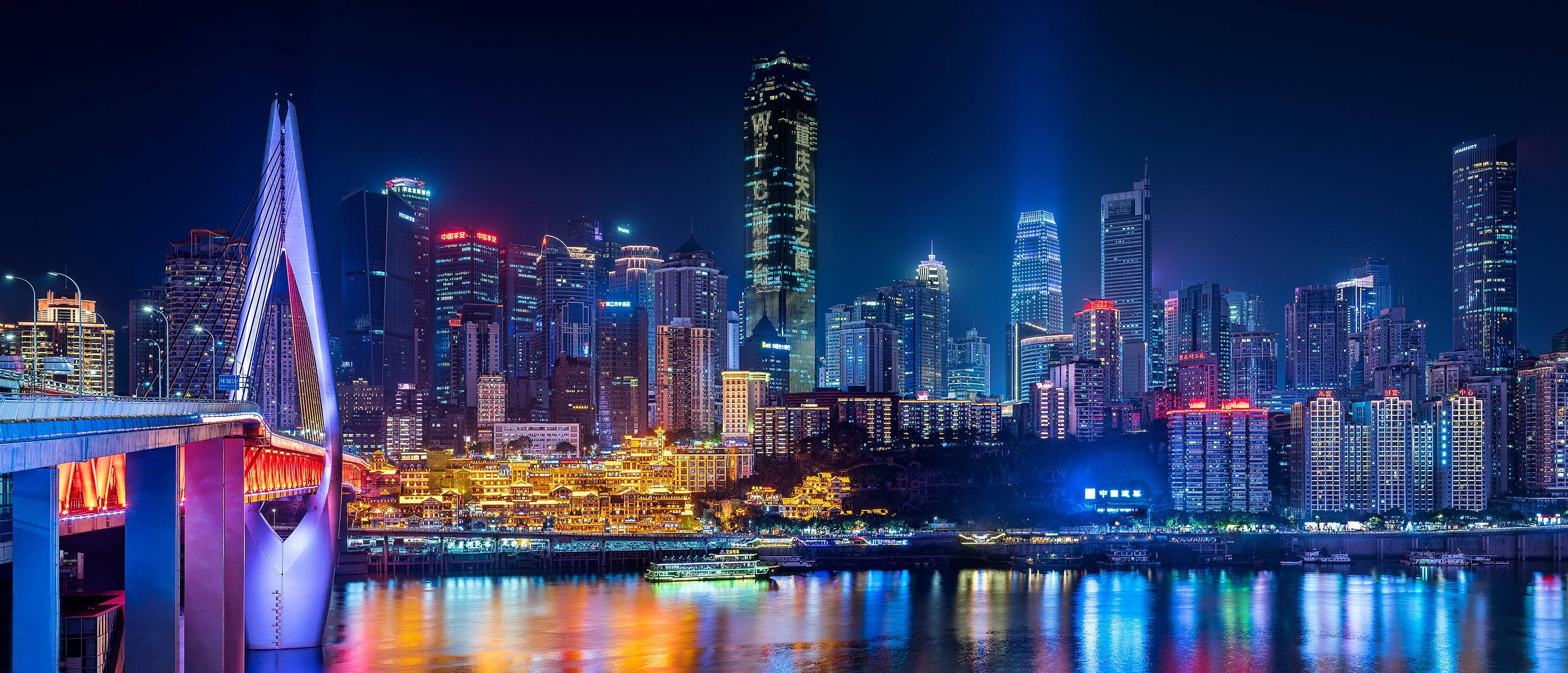 Chongqing 桌布 壁紙 — 一個耀眼的夜景城市景觀，發光的橋樑和摩天大樓倒映在充滿活力的河流中。