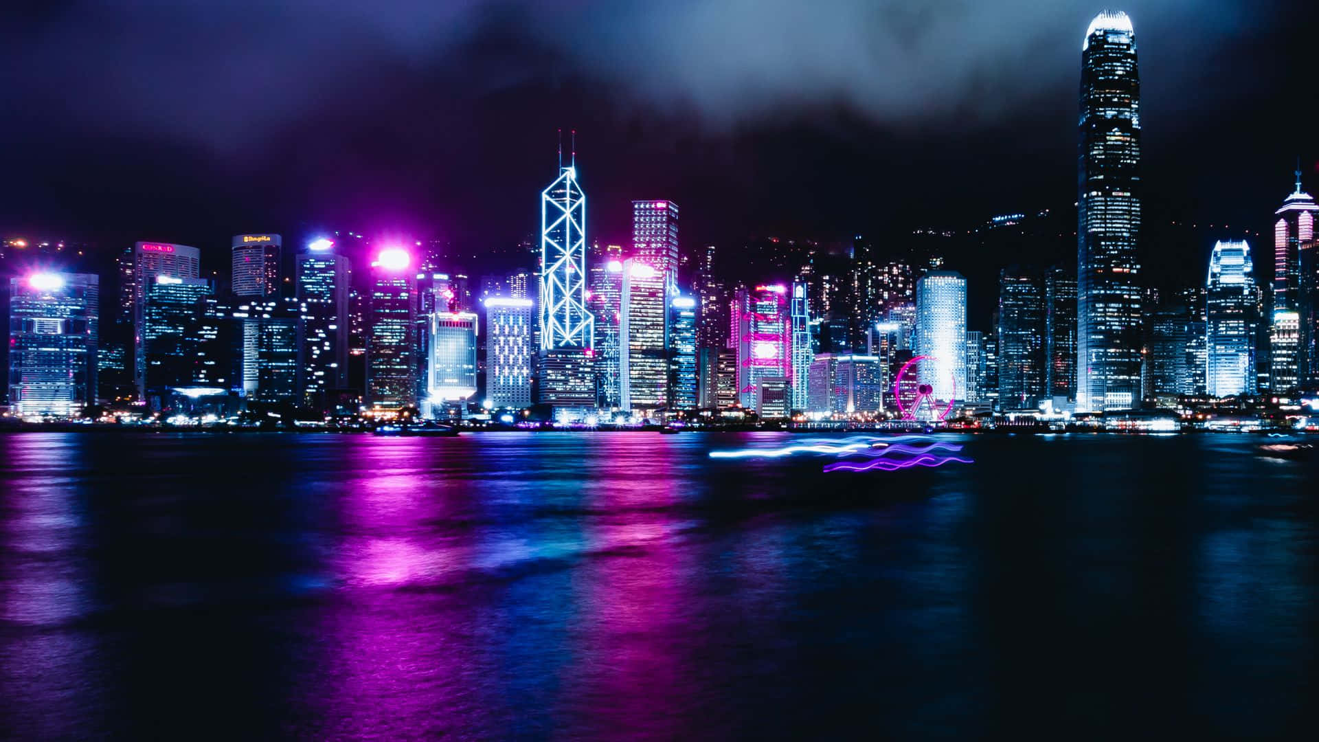 Epic Neon 桌布 壁紙 — 一個耀眼的夜景城市景觀，霓虹燈閃爍的摩天大樓在平靜的水面上反射出充滿活力的紫色和藍色燈光。