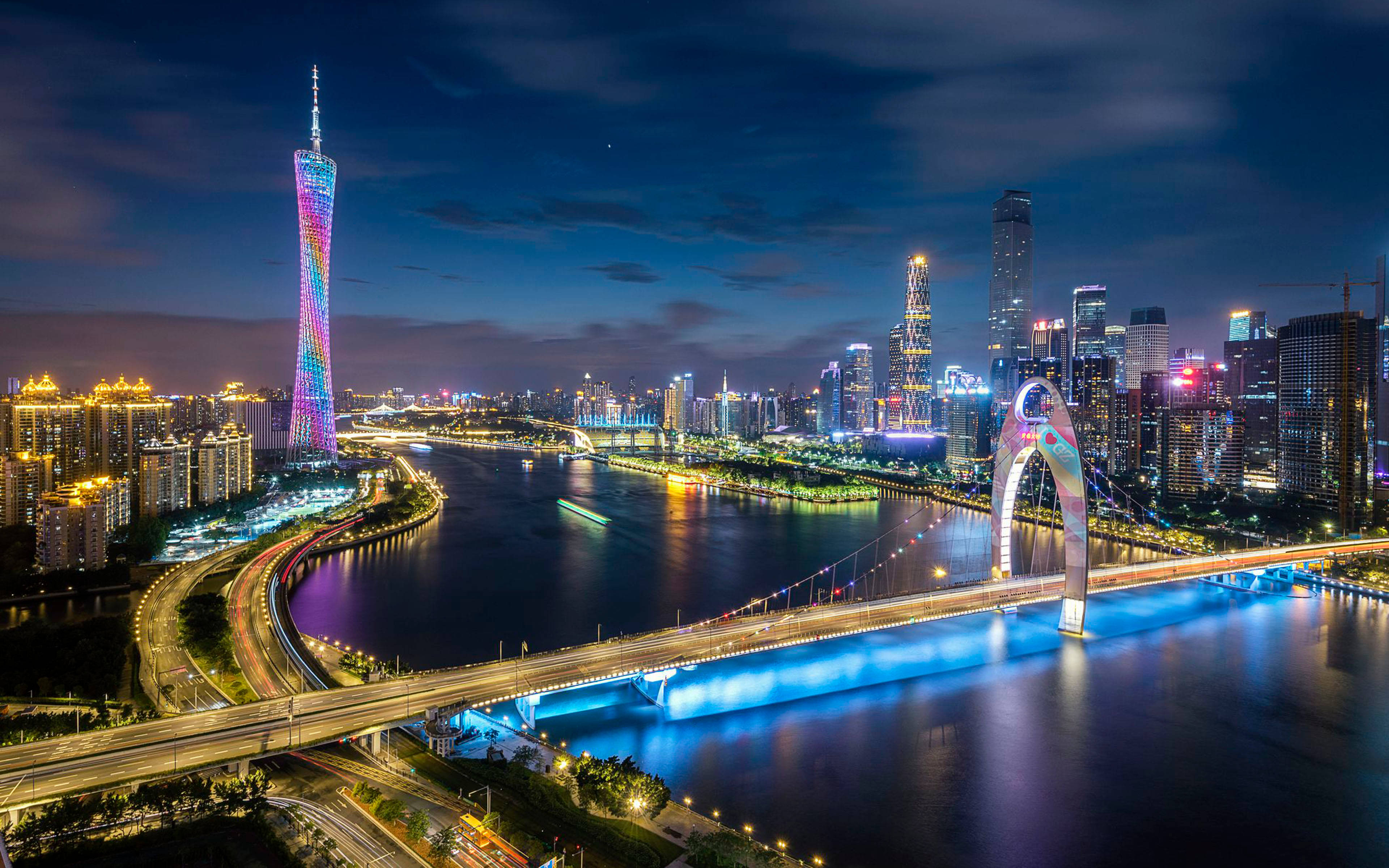 Guangzhou 桌布 壁紙 — 一個耀眼的夜間城市景觀，特色是發光的塔樓和橫跨河流的照明橋樑，帶有交通痕跡。