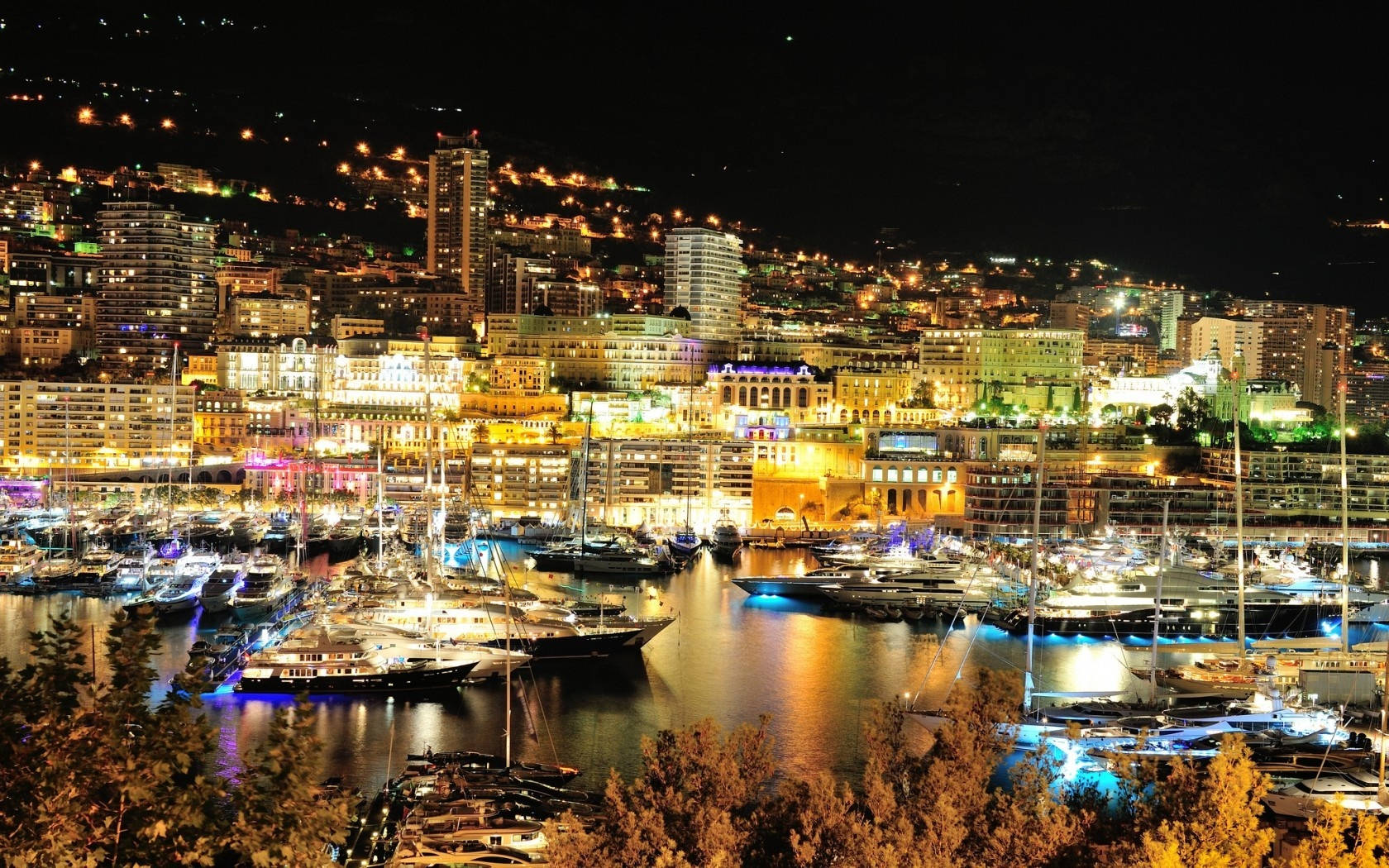 Monaco 桌布 壁紙 — 一個耀眼的夜間海港場景，閃爍的城市燈光倒映在停滿豪華遊艇和船隻的水面上。