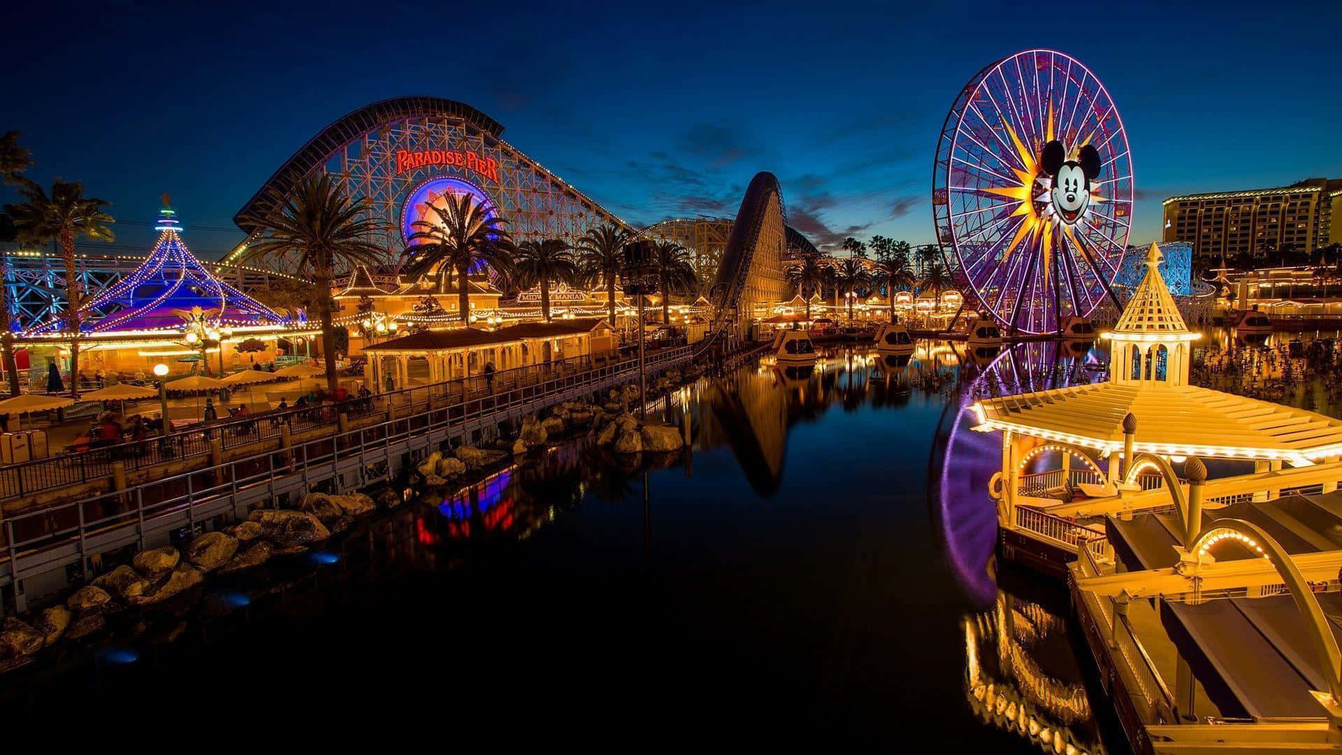 Disneyland 桌布 壁紙 — 一個耀眼的夜間遊樂園，有發光的米奇老鼠摩天輪和雲霄飛車倒映在平靜的水面上。