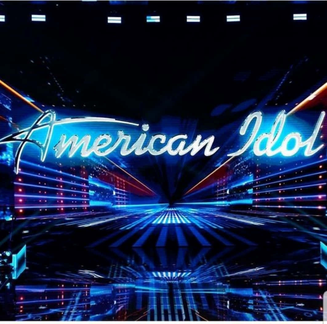 american idol 桌布 壁紙 — 一個耀眼的藍色「American Idol」霓虹標誌在充滿未來感的舞台上閃耀，配以雷射燈光和反光地板。