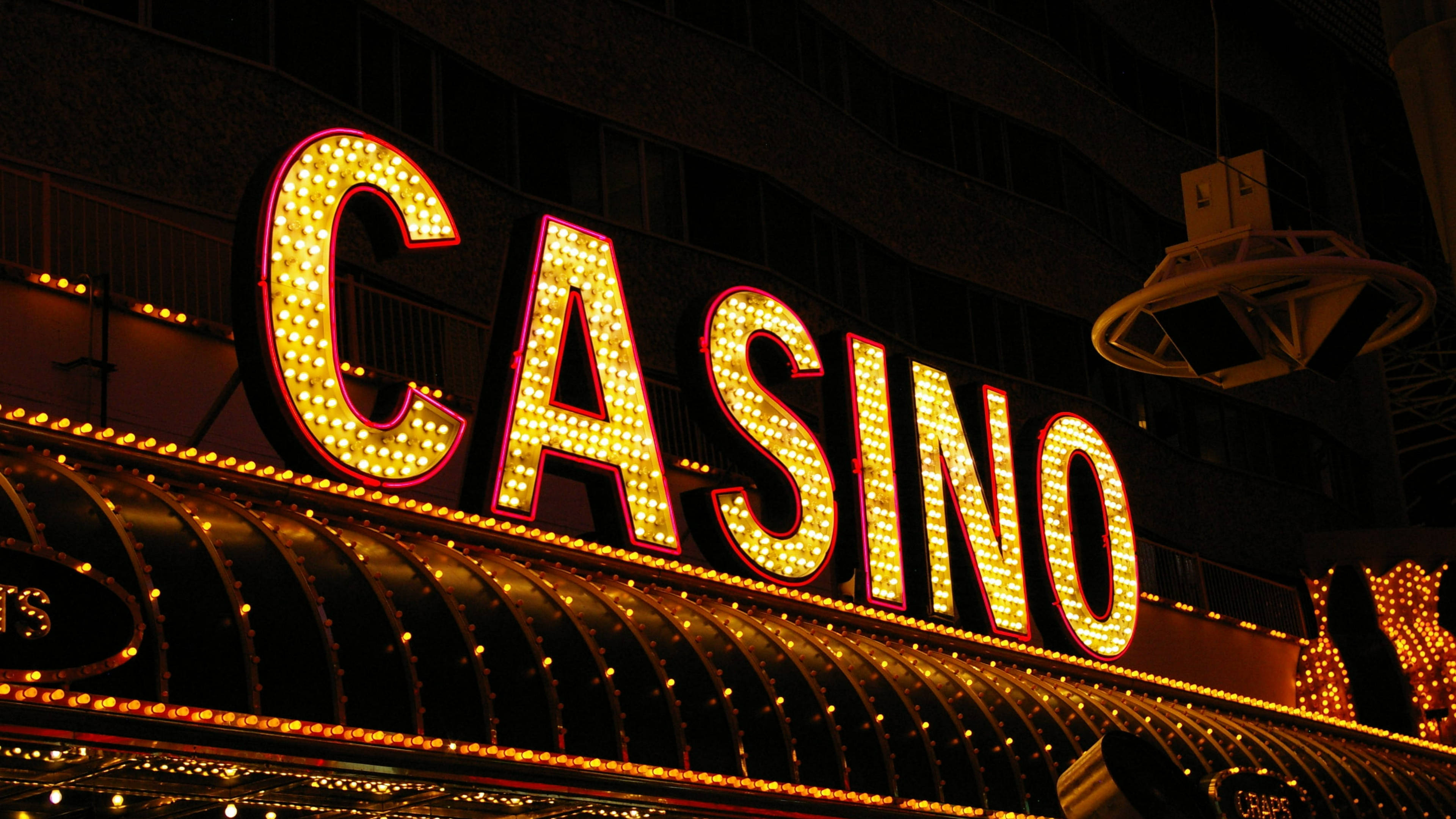 拉斯維加斯 桌布 壁紙 — 一個耀眼的霓虹燈「CASINO」招牌在漆黑的都市夜空下溫暖地發光，下方有彎曲的遮陽篷。