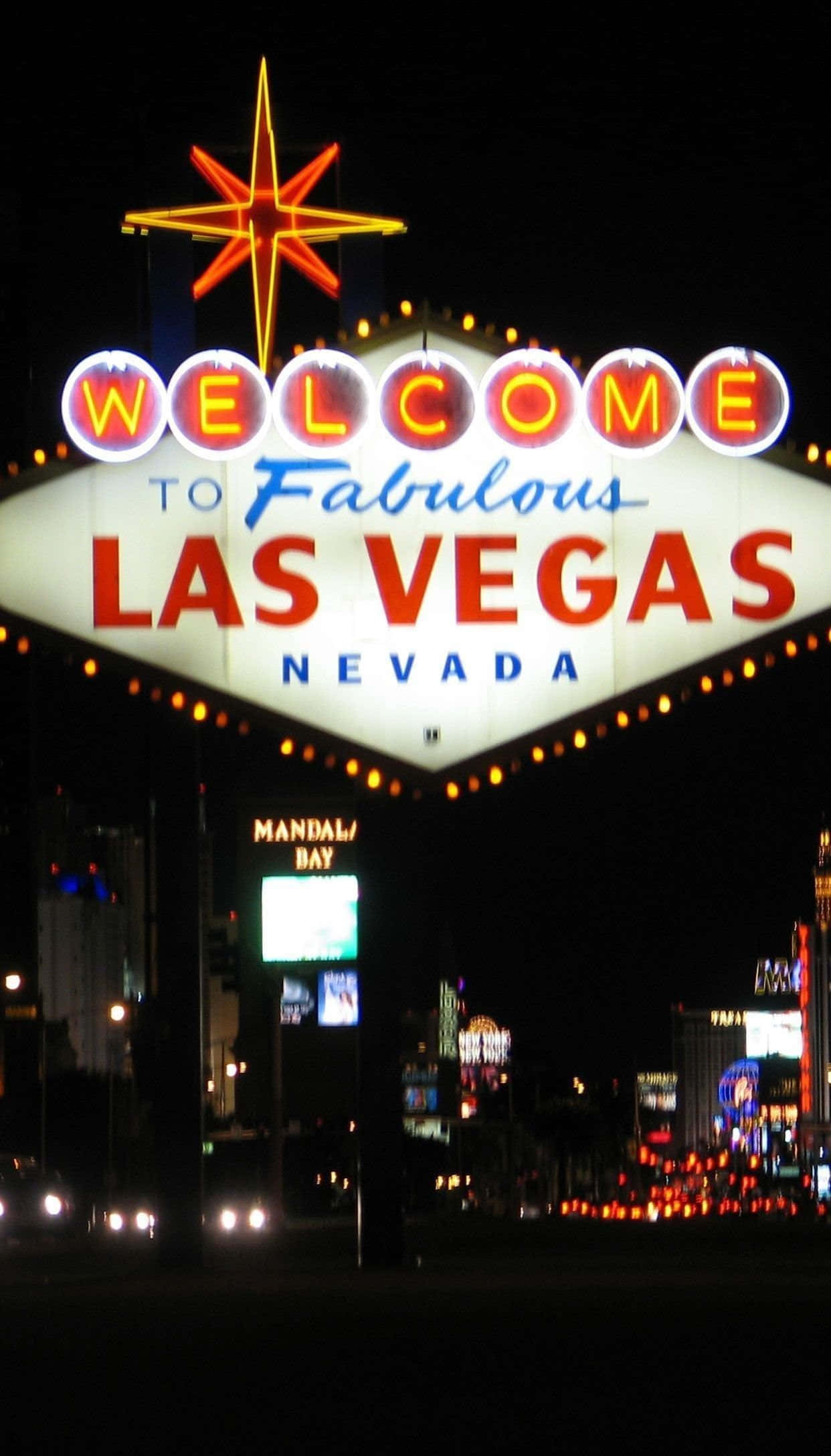 Nevada 桌布 壁紙 — 一個耀眼的霓虹燈牌「Welcome to Fabulous Las Vegas Nevada」在夜間發光，襯托著黑暗的天空和下方的城市燈光。