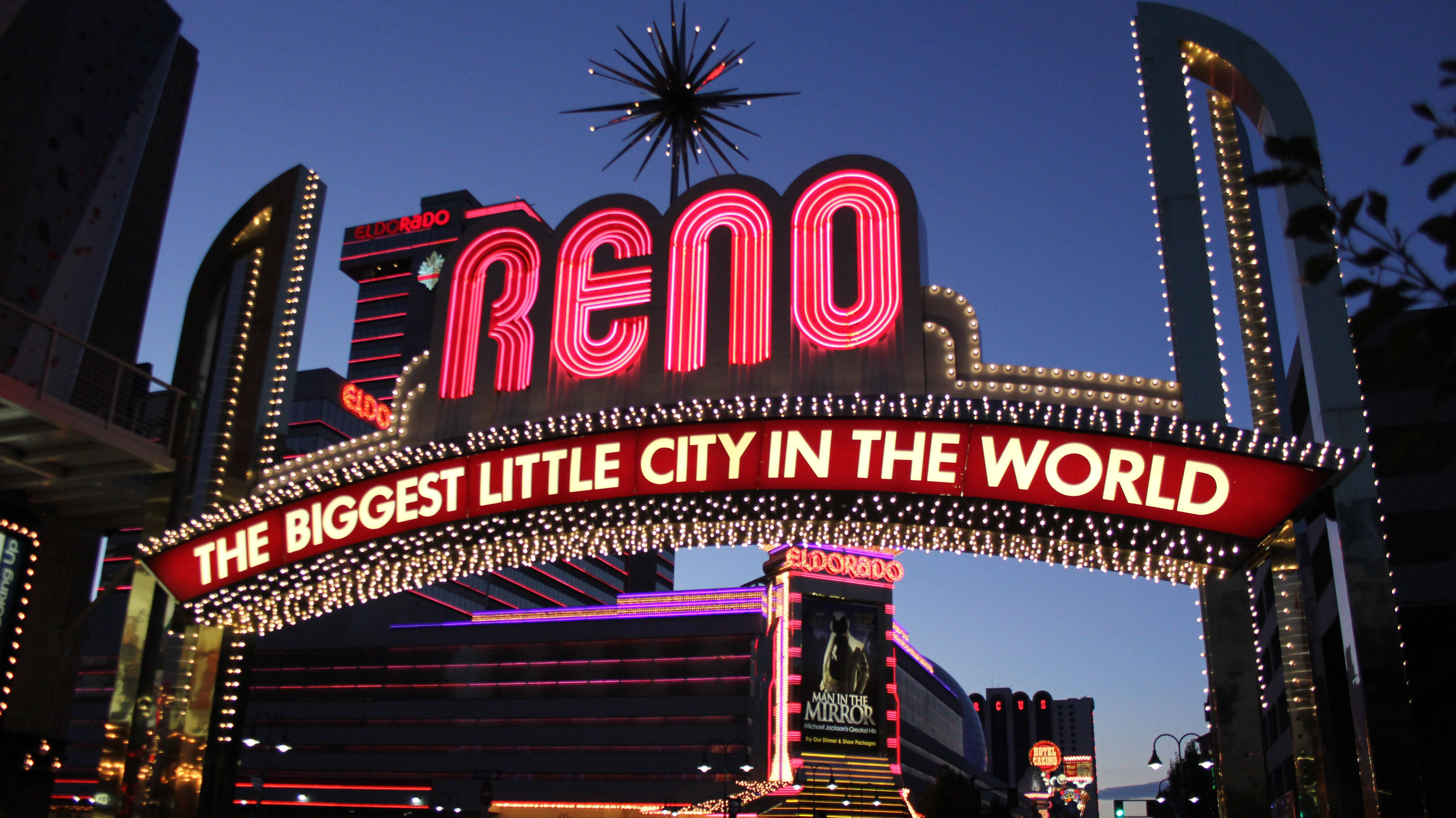Arch 桌布 壁紙 — 一個耀眼的霓虹燈牌，上面寫著「RENO THE BIGGEST LITTLE CITY IN THE WORLD」，在暮色天空下閃耀，映襯著繁華的城市景象。