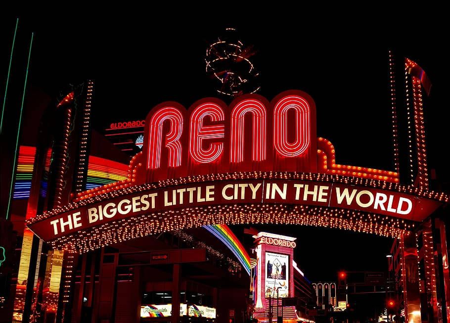 City Night 桌布 壁紙 — 一個耀眼的霓虹燈牌，上面寫著「RENO THE BIGGEST LITTLE CITY IN THE WORLD」，在漆黑的夜空下發出紅光，下方有彩虹燈光。