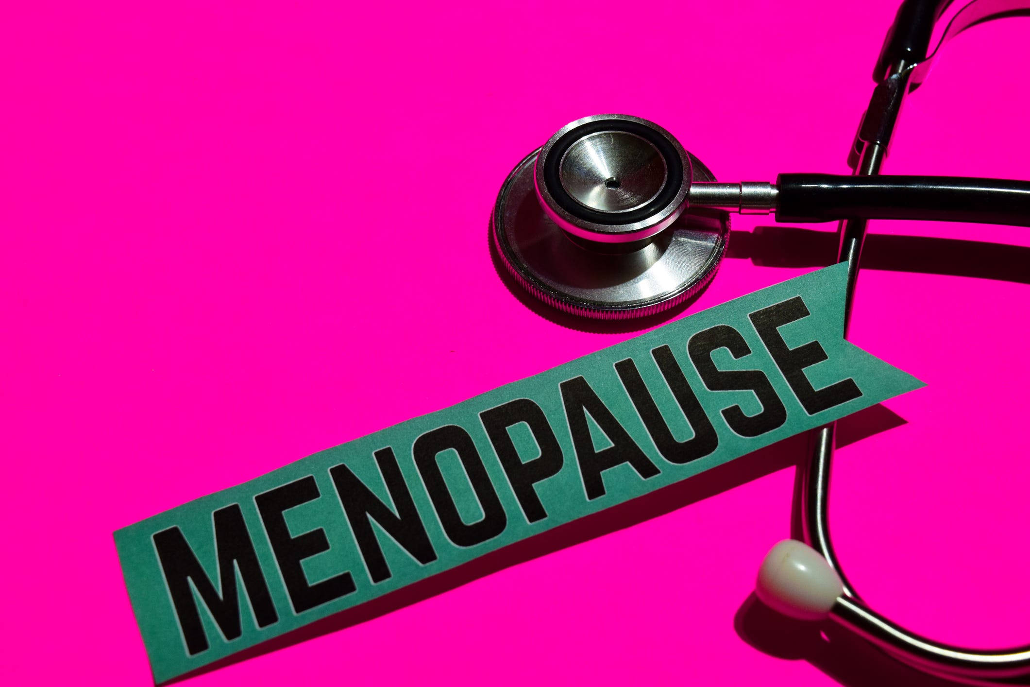 Menopause 桌布 壁紙 — 一個聽診器放在一個綠色橫幅旁邊，上面寫著 'MENOPAUSE'，背景是鮮豔的粉紅色。