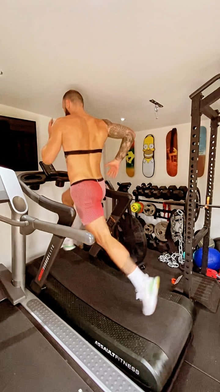 Fitness 桌布 壁紙 — 一個肌肉男在設有啞鈴和滑板掛牆的家用健身房的跑步機上跑步。