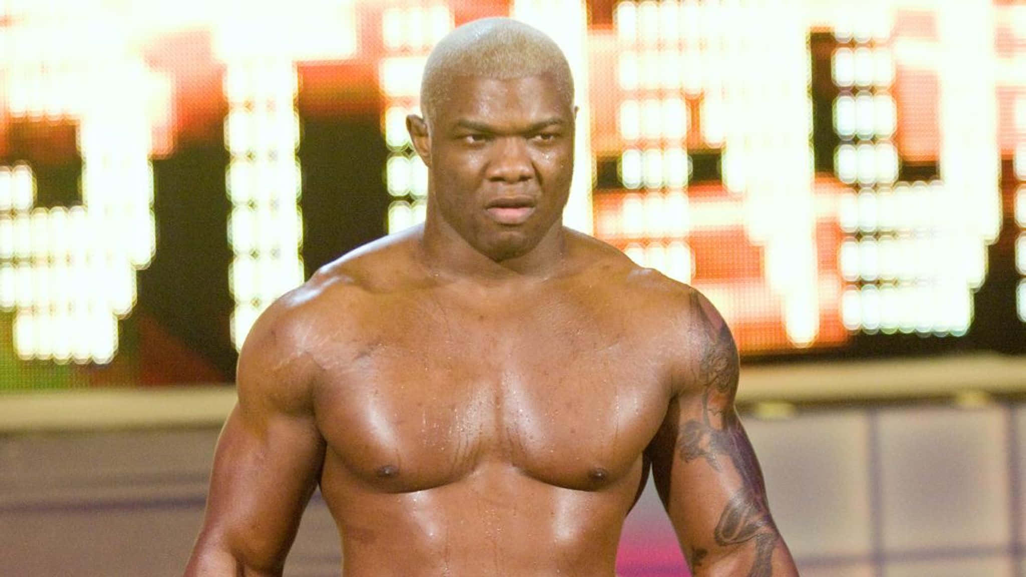 WWE 桌布 壁紙 — 一個肌肉發達、光頭、有刺青的男人在明亮的競技場燈光下凝視著鏡頭。