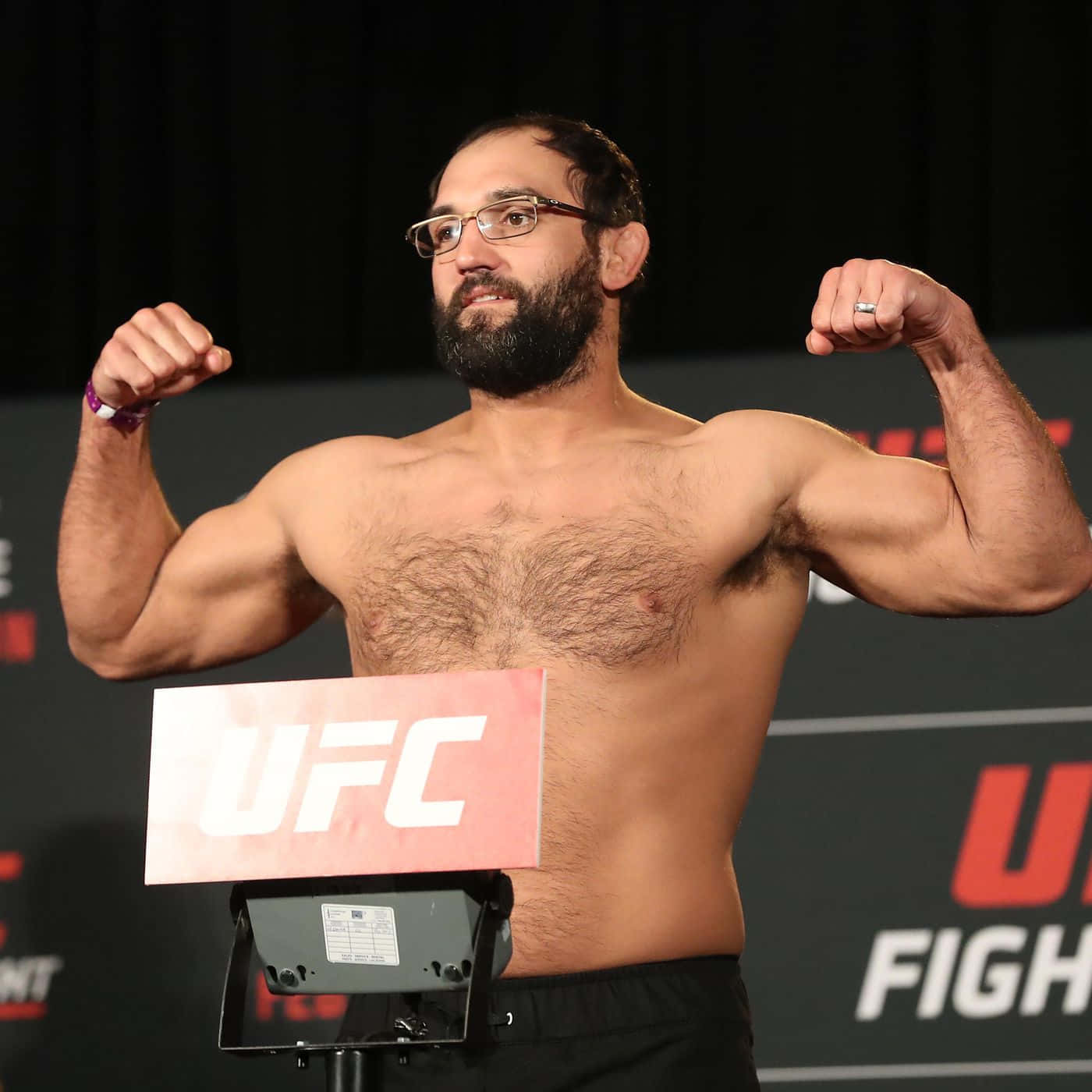 UFC 桌布 壁紙 — 一個肌肉發達、戴眼鏡的鬍鬚男在黑暗背景下於UFC磅上彎曲雙臂。