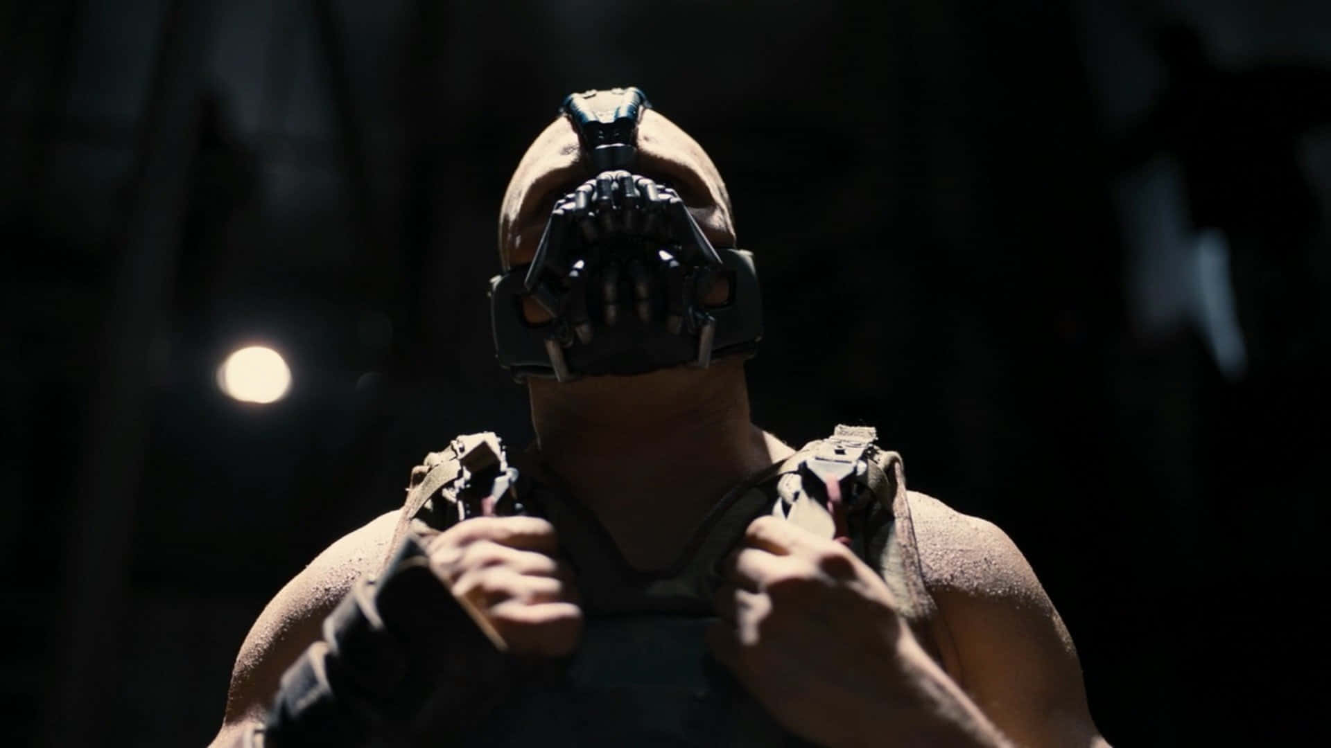 bane 桌布 壁紙 — 一個肌肉發達、戴著蝙蝠面具的男人站在陰影黑暗中，單一聚光燈凸顯他強烈的目光和裝甲的肩膀。