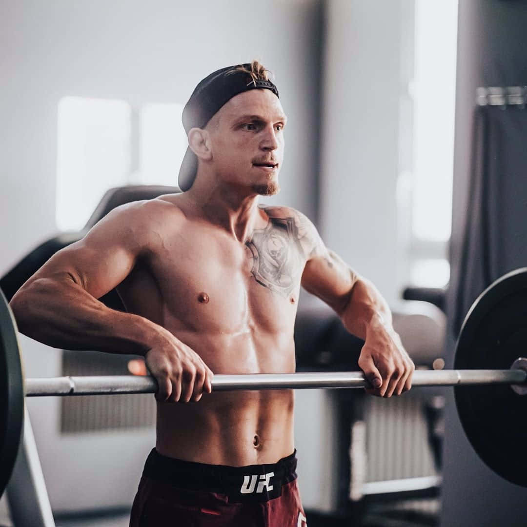 Fitness 桌布 壁紙 — 一個肌肉發達、手臂有刺青的男人在明亮的健身房裡抓住槓鈴，專注並準備舉起。