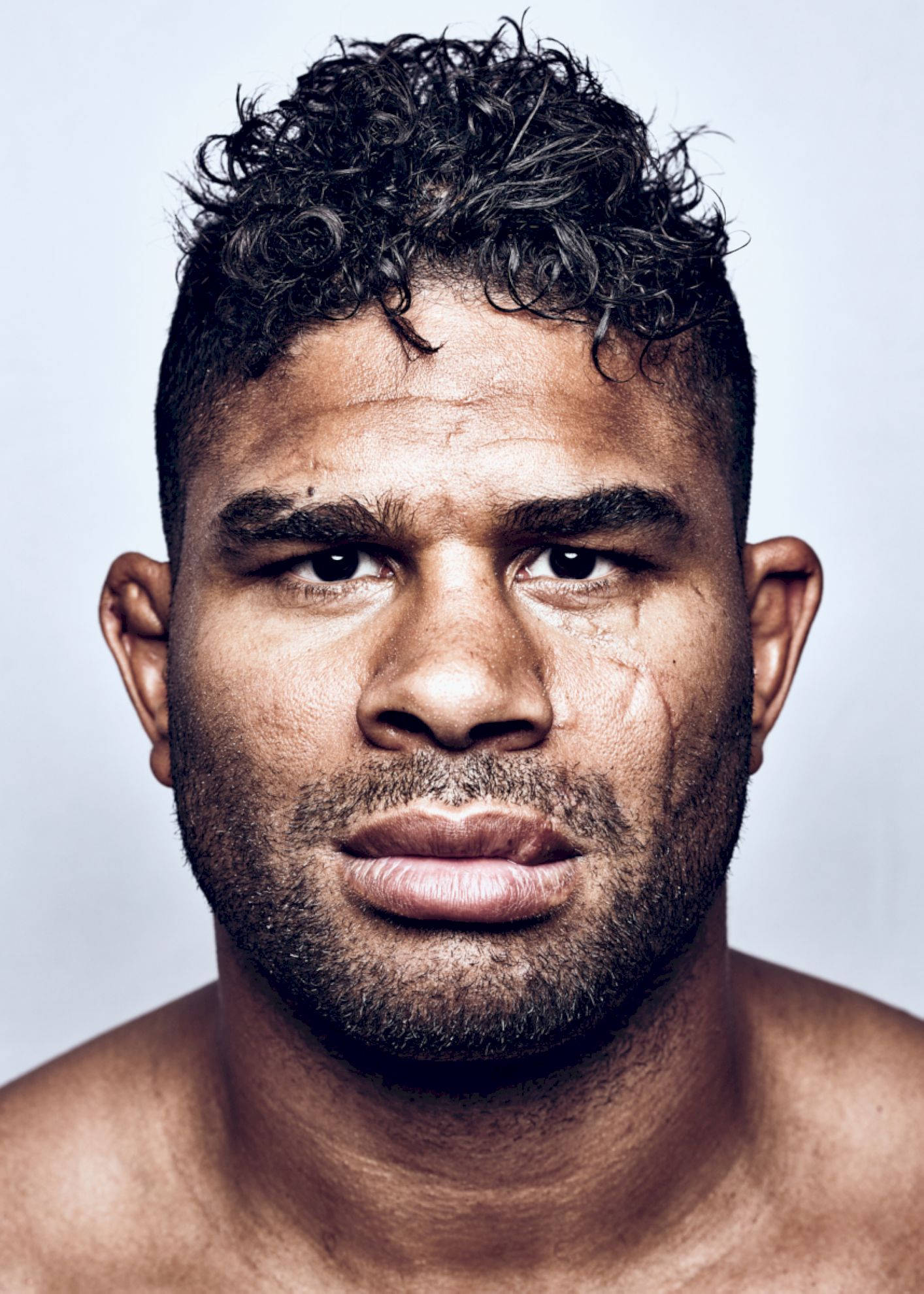 UFC 桌布 壁紙 — 一個肌肉發達、擁有深色捲髮和專注強烈眼神的男子，在純淺灰色背景前的特寫肖像。