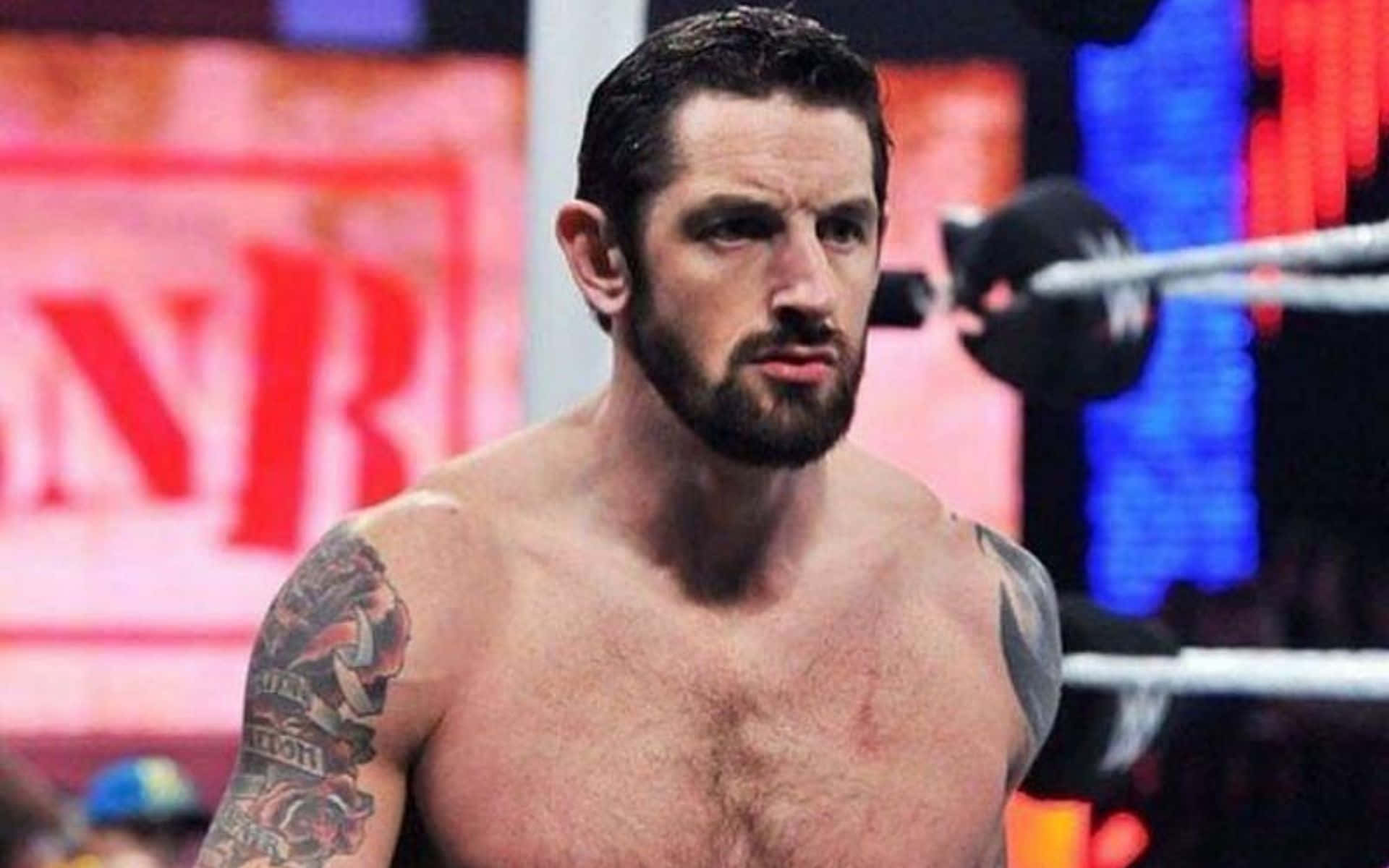 WWE 桌布 壁紙 — 一個肌肉發達、有刺青、留鬍子的摔角手在燈光璀璨的擂台上，背後有紅藍燈光，眼神銳利。