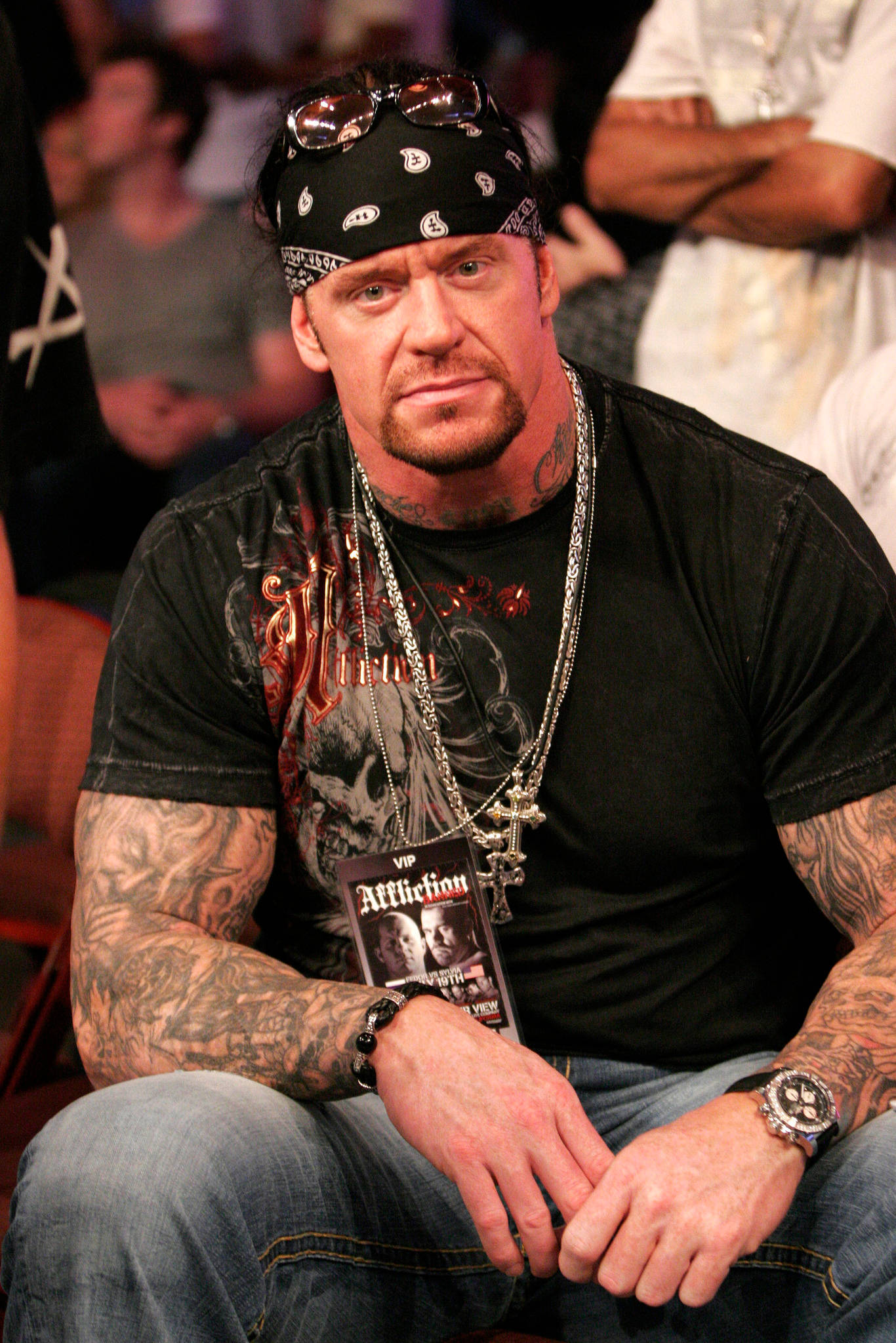 Undertaker 桌布 壁紙 — 一個肌肉發達、有刺青和戴頭巾的男人坐在人群中，手持VIP通行證。