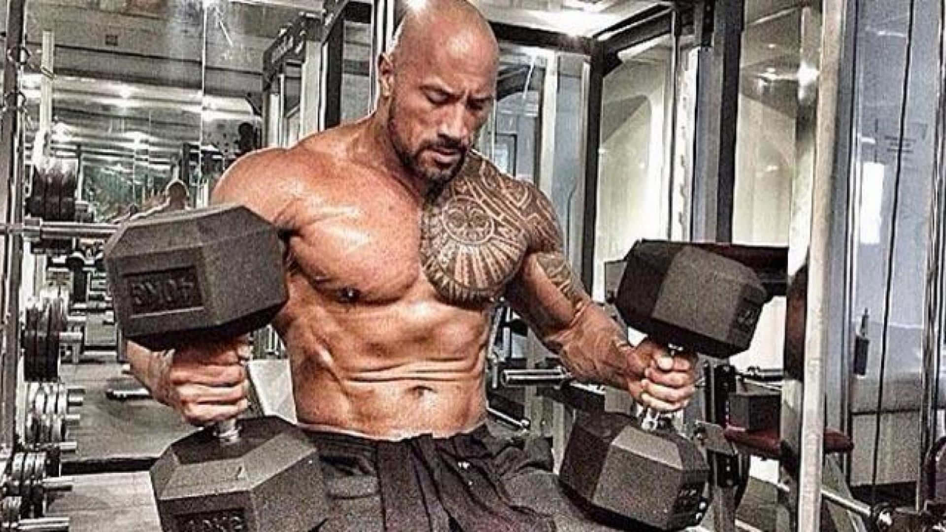 The Rock 桌布 壁紙 — 一個肌肉發達、有刺青的光頭男子在明亮的健身房裡舉起沉重的啞鈴，健身房有鏡面牆壁和重量架。