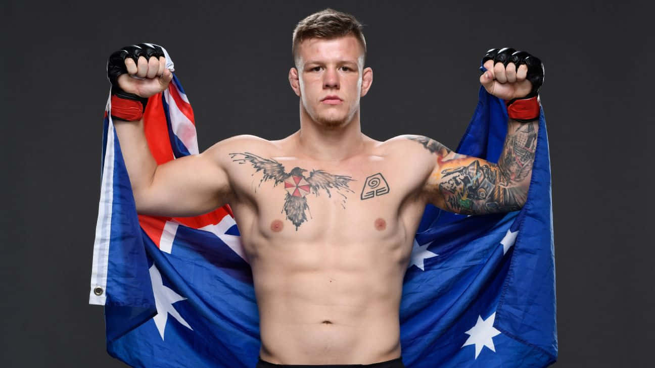 UFC 桌布 壁紙 — 一個肌肉發達、有刺青的戰士，在黑暗背景下以強而有力的姿勢將澳洲國旗披在肩上。