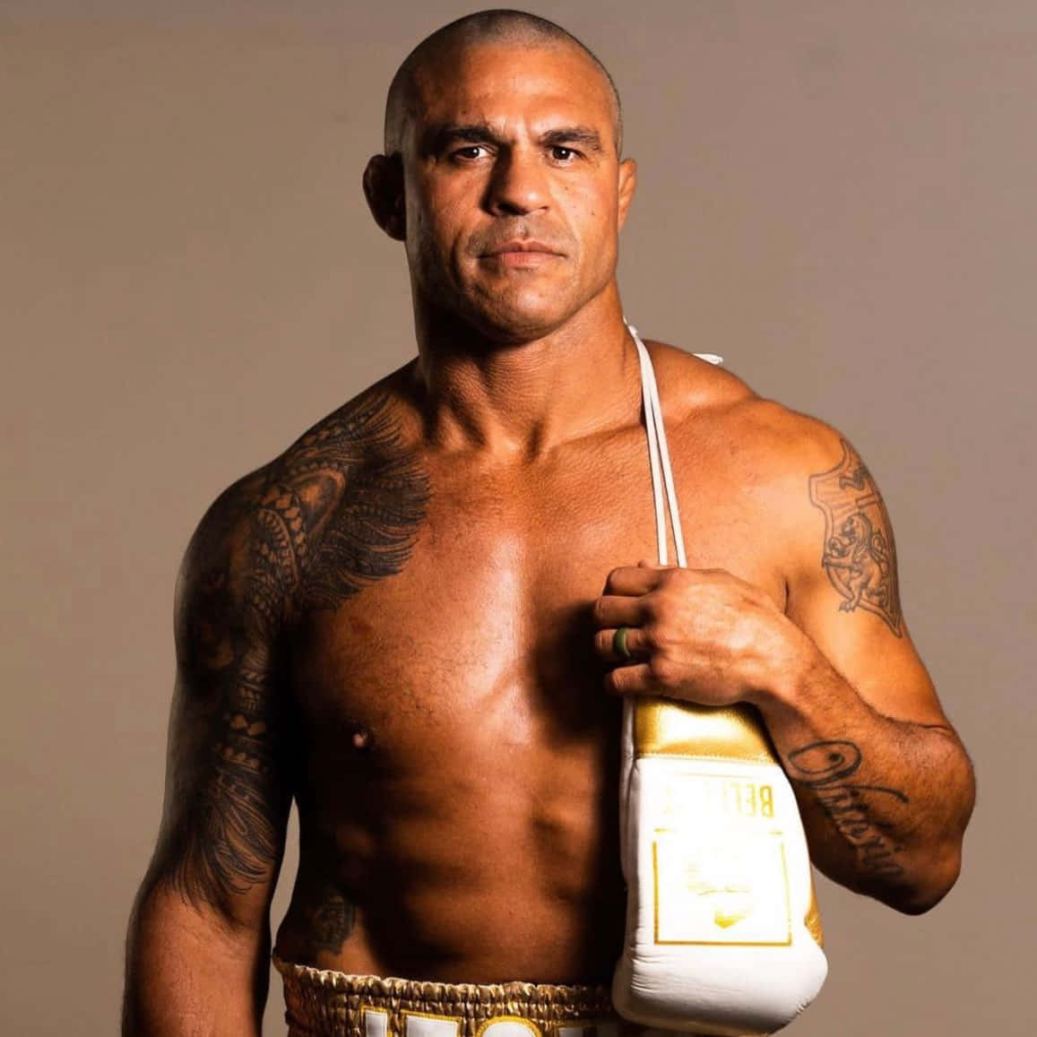 Boxing 桌布 壁紙 — 一個肌肉發達、有刺青的拳擊手，在一個中性的攝影棚背景下，手持白色和金色的拳擊手套，眼神專注。