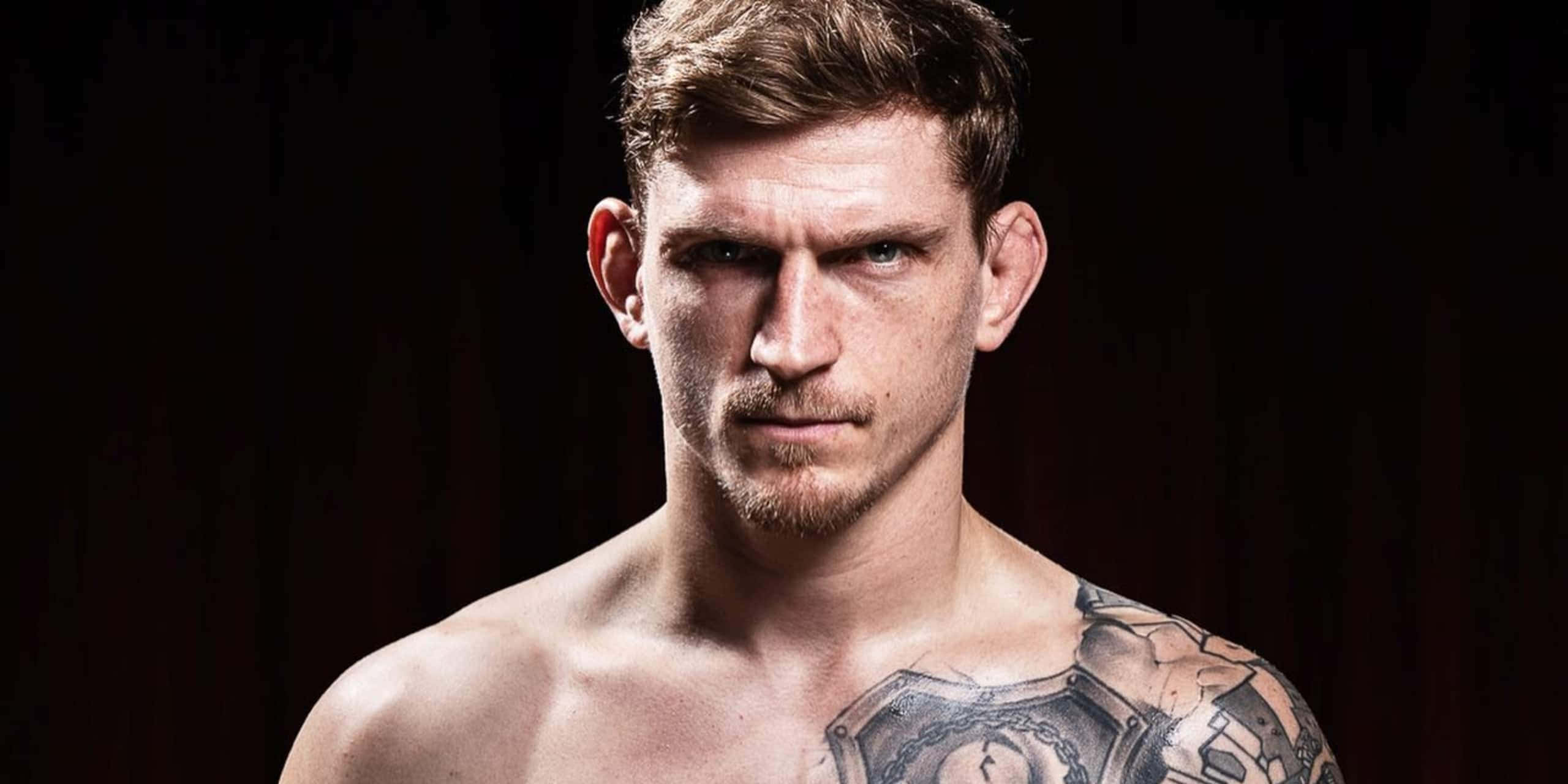 UFC 桌布 壁紙 — 一個肌肉發達、有刺青的男人在黑暗背景下強烈地凝視。