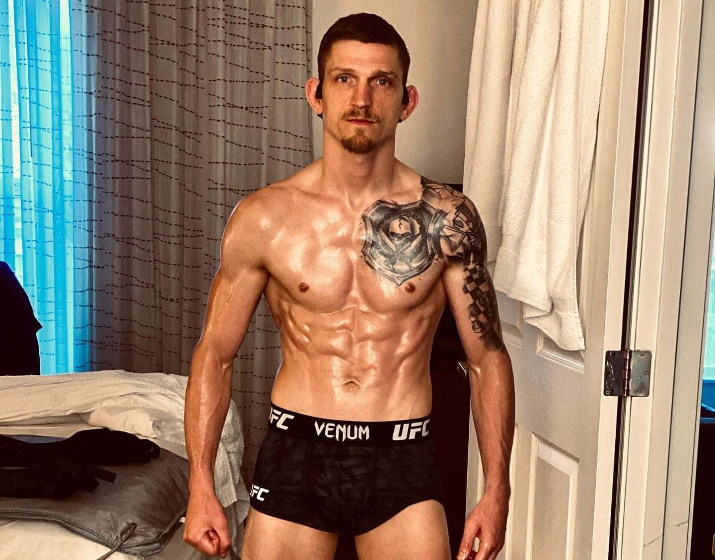 UFC 桌布 壁紙 — 一個肌肉發達、有玫瑰刺青的男人在飯店房間赤裸上身，穿著UFC品牌的內衣。