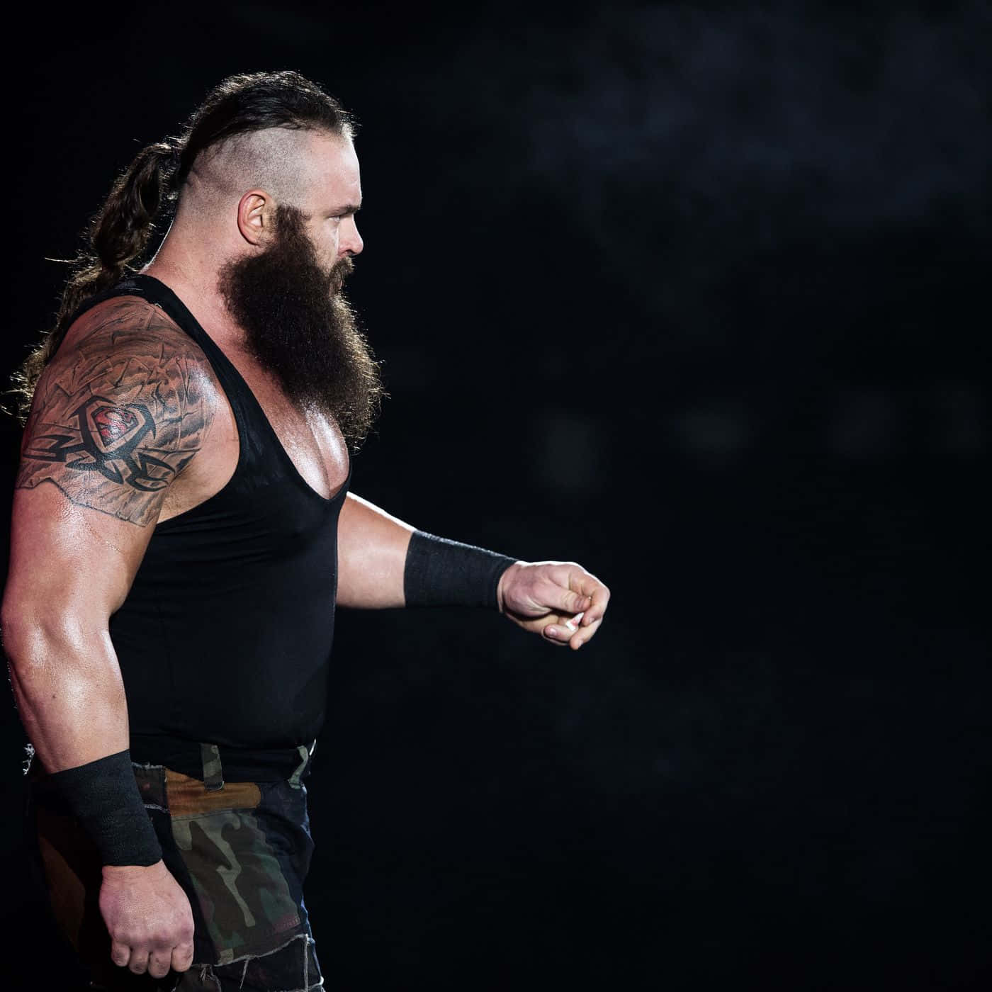 WWE 桌布 壁紙 — 一個肌肉發達、有鬍鬚、手臂有刺青的摔角手，穿著黑色背心，在黑暗煙霧繚繞的背景中向前邁進。