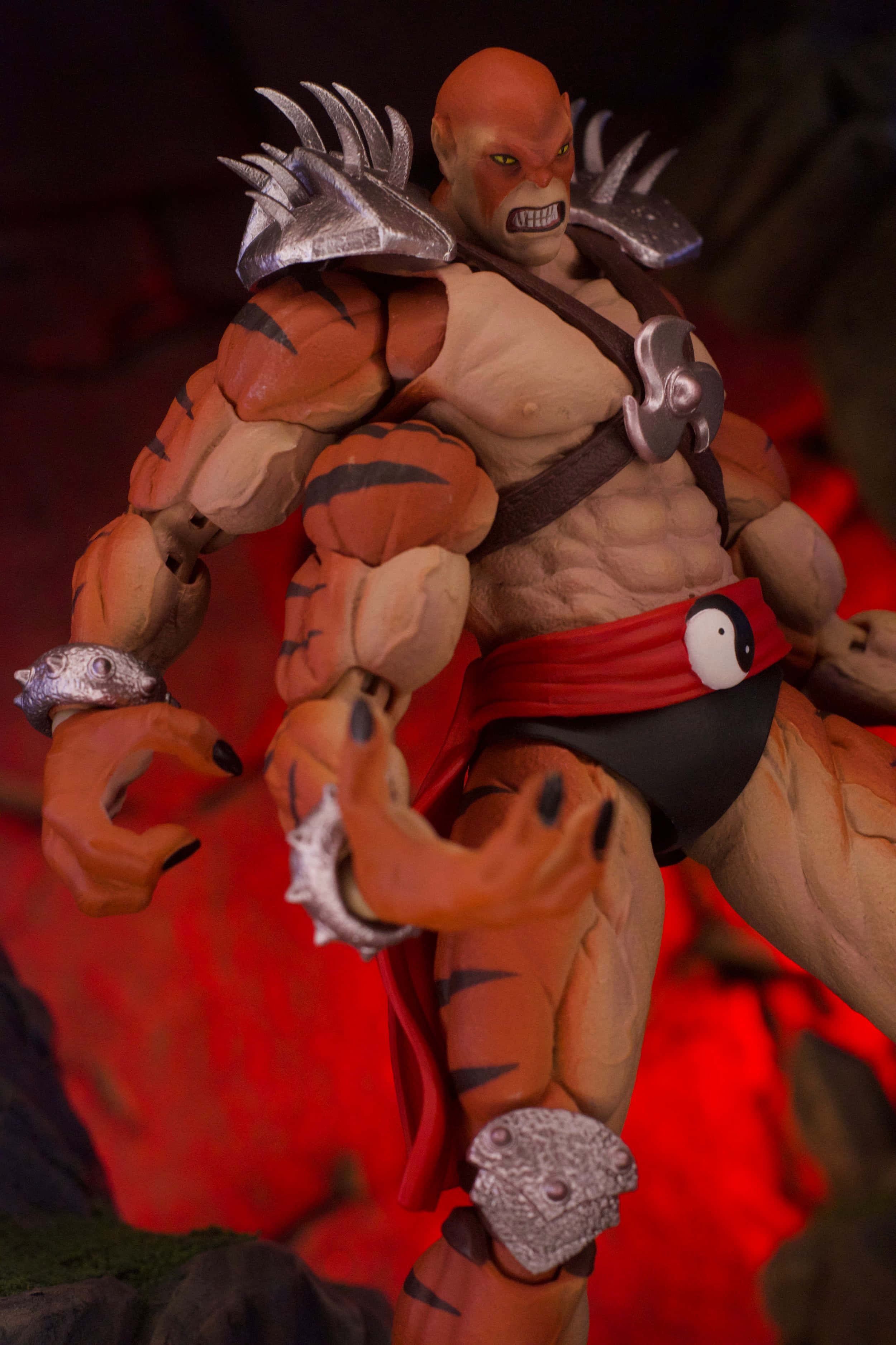 Mortal Kombat Kintaro 桌布 壁紙 — 一個肌肉發達、橙色皮膚、帶有老虎條紋和銀色盔甲的可動人偶，在發光的紅色背景前擺出兇猛的姿勢。